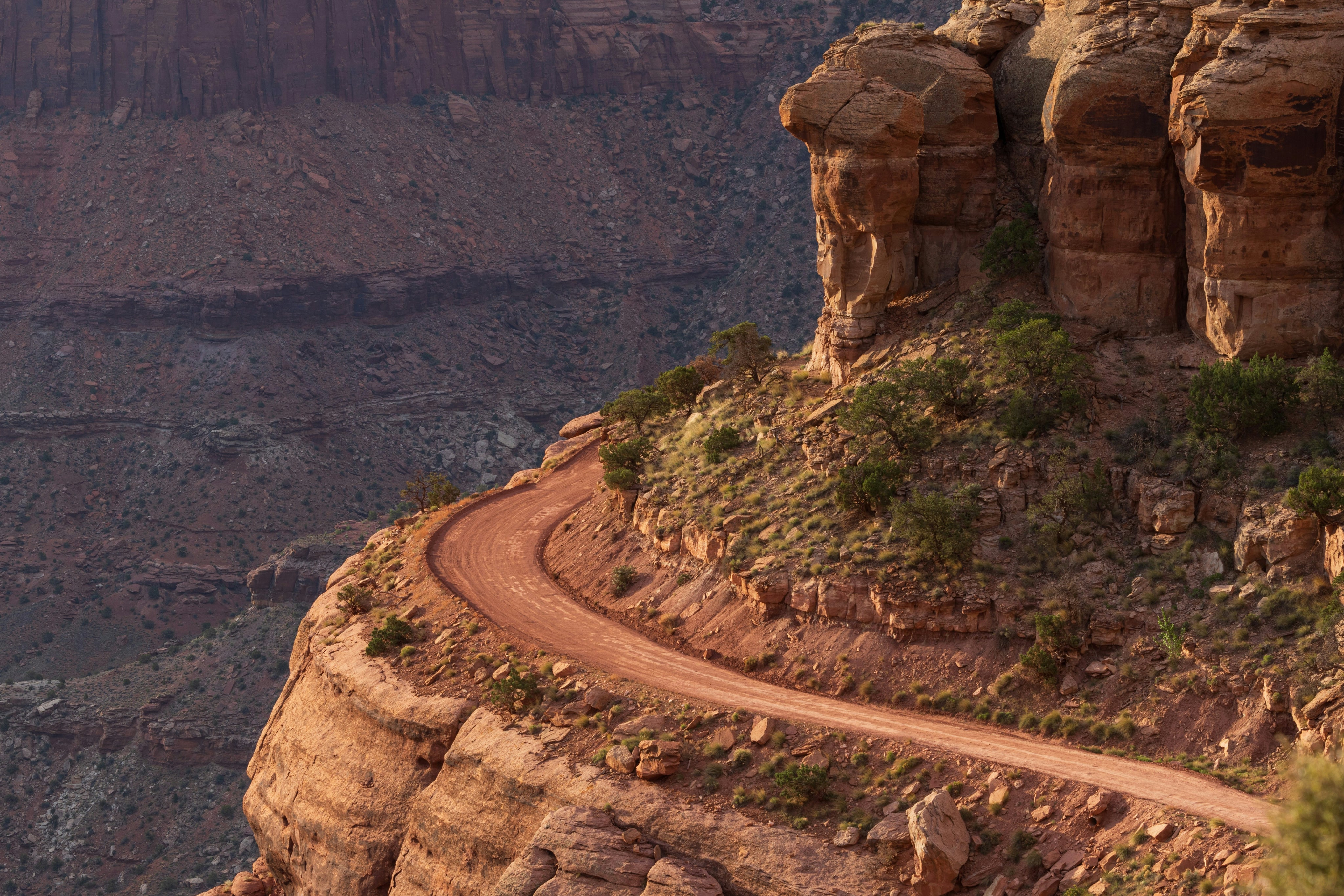 Dirt road winding along the edge of a steep red rock canyon cliff