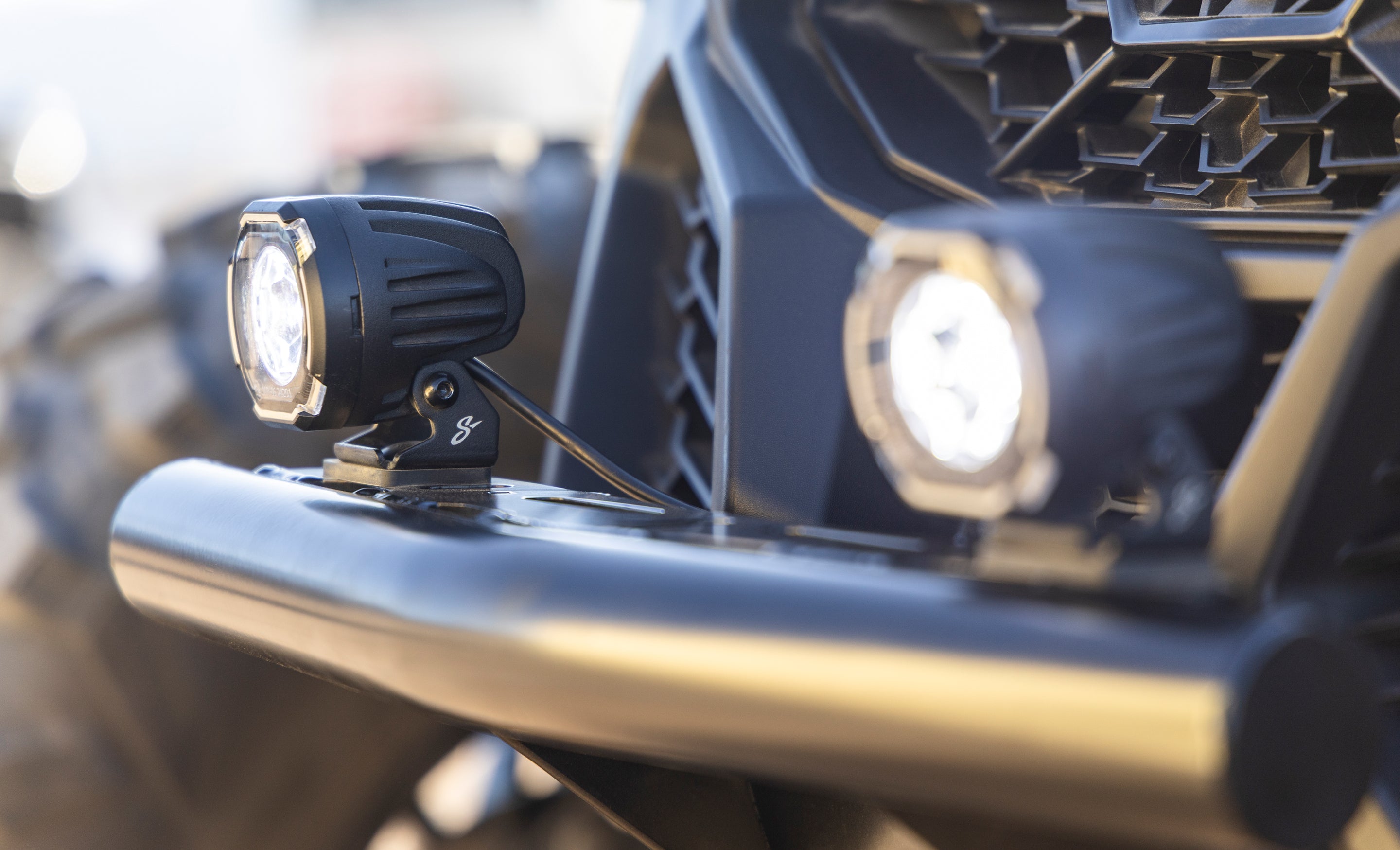 Two round LED off road lights mounted on a black vehicle bumper