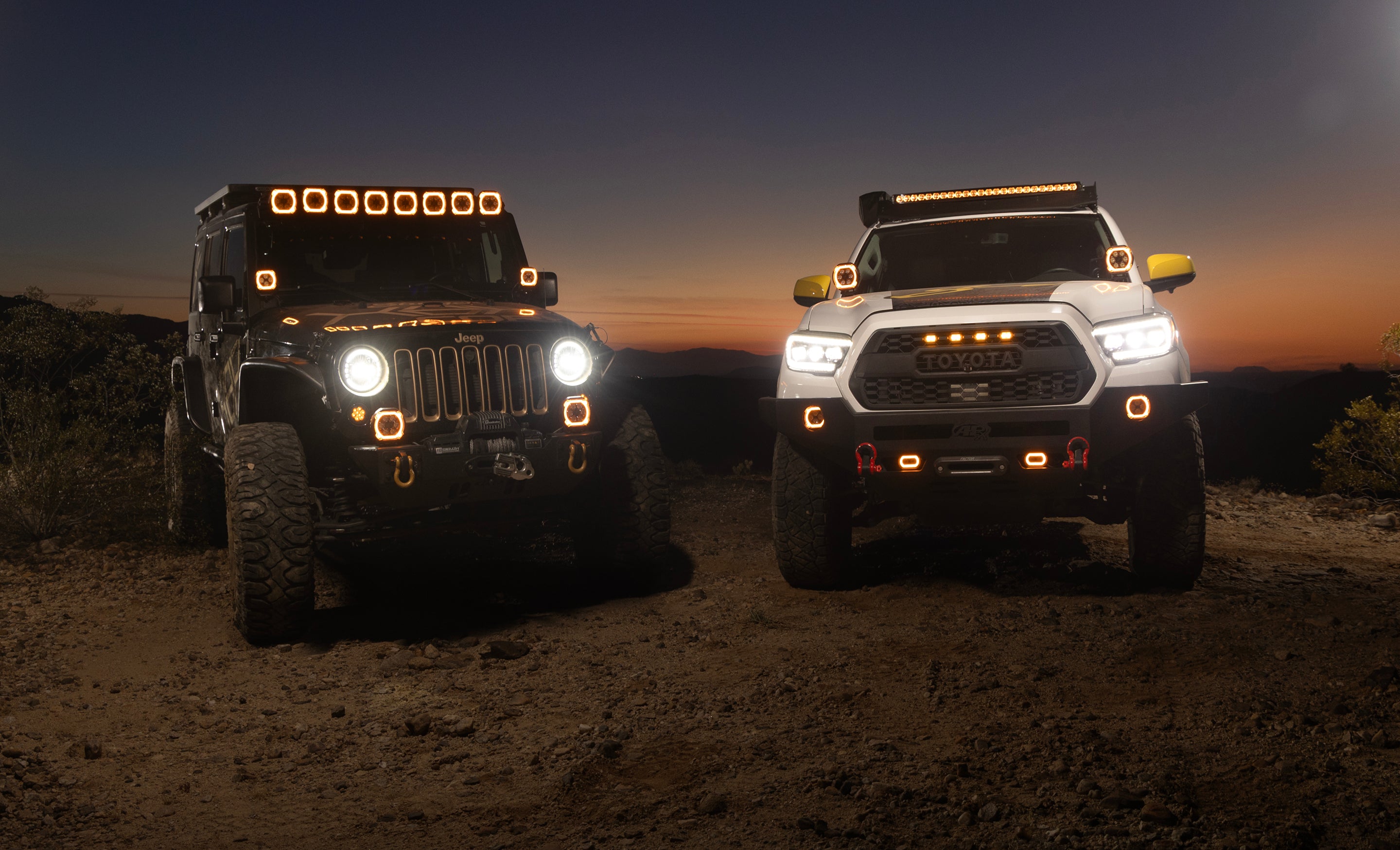 Black Jeep and white Toyota off road trucks parked at sunset with illuminated LED lights
