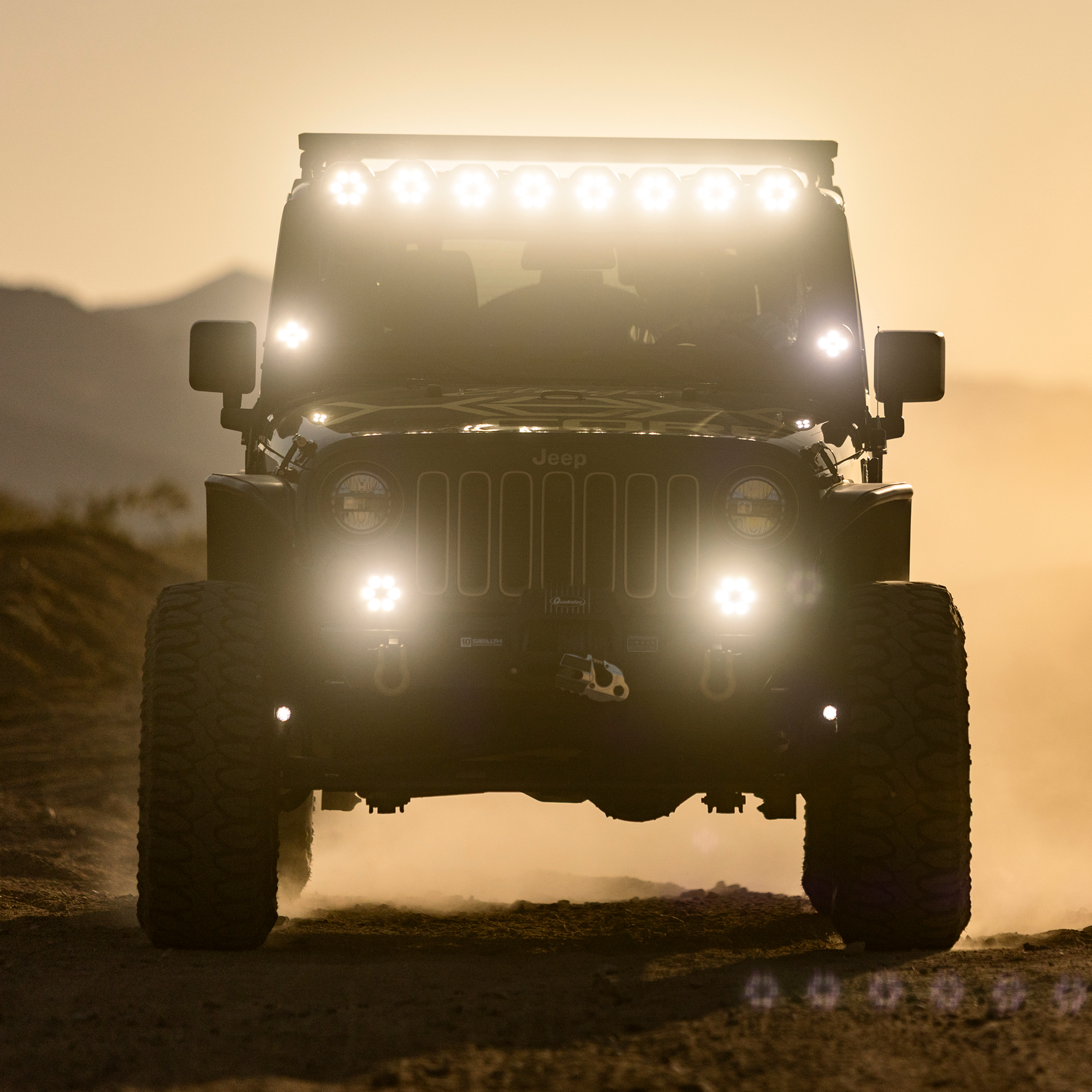 Jeep Wrangler with off road lights illuminated on a dusty trail at sunset