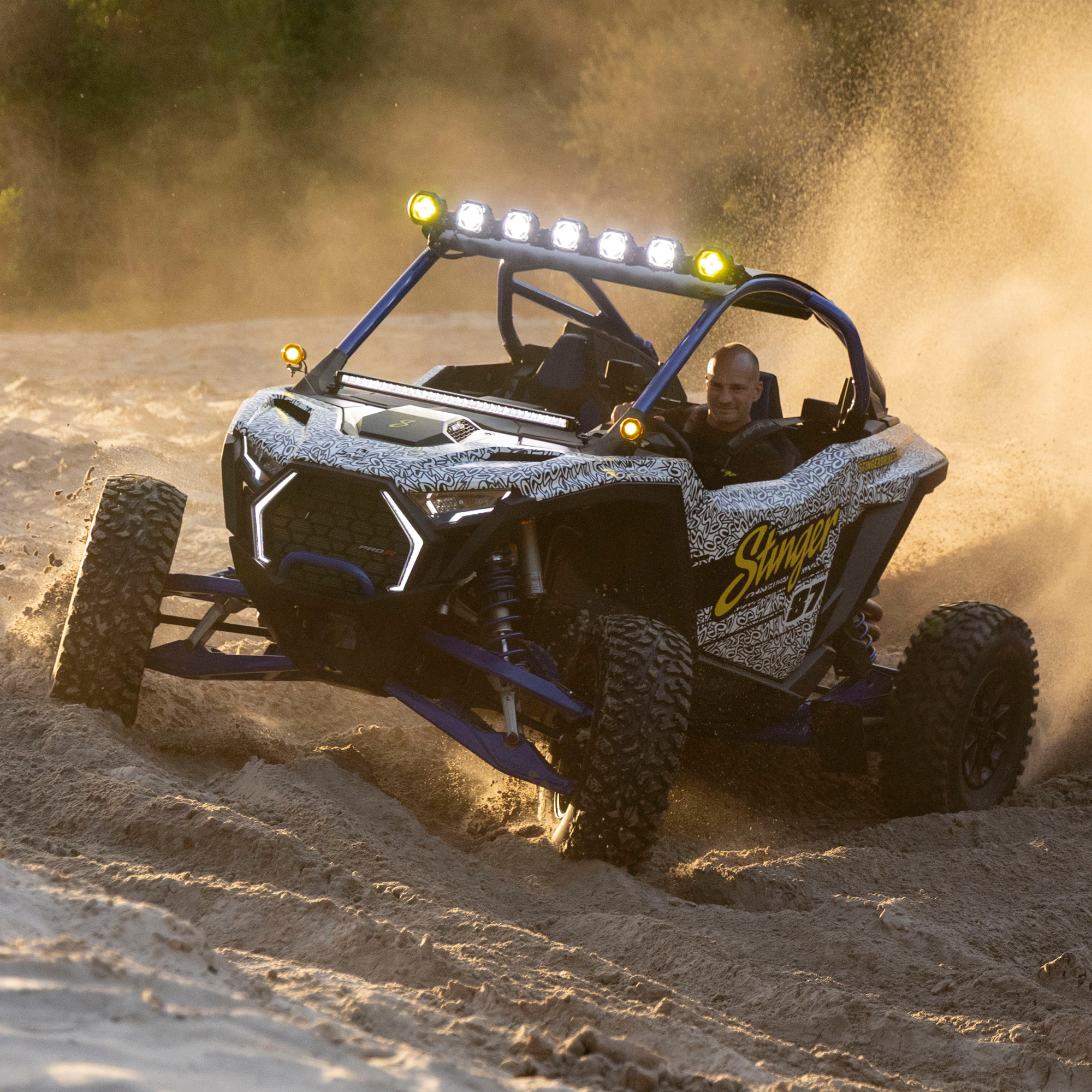 Driver in a patterned off road vehicle kicking up sand on a dune