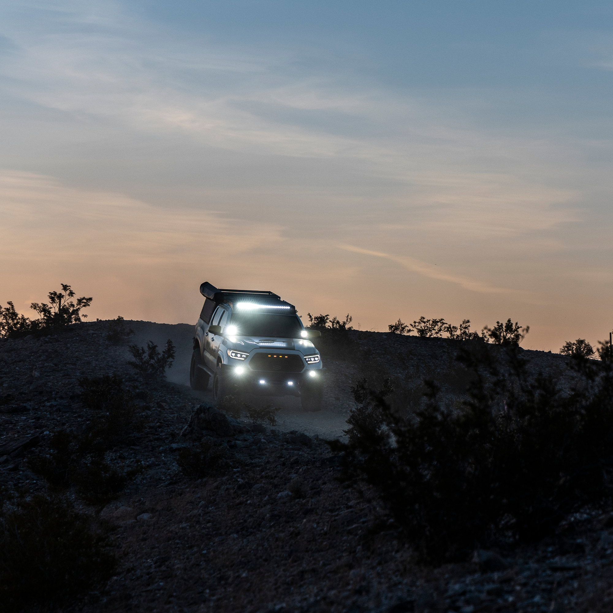 Off road truck with roof rack and LED lights driving on a desert trail at sunset