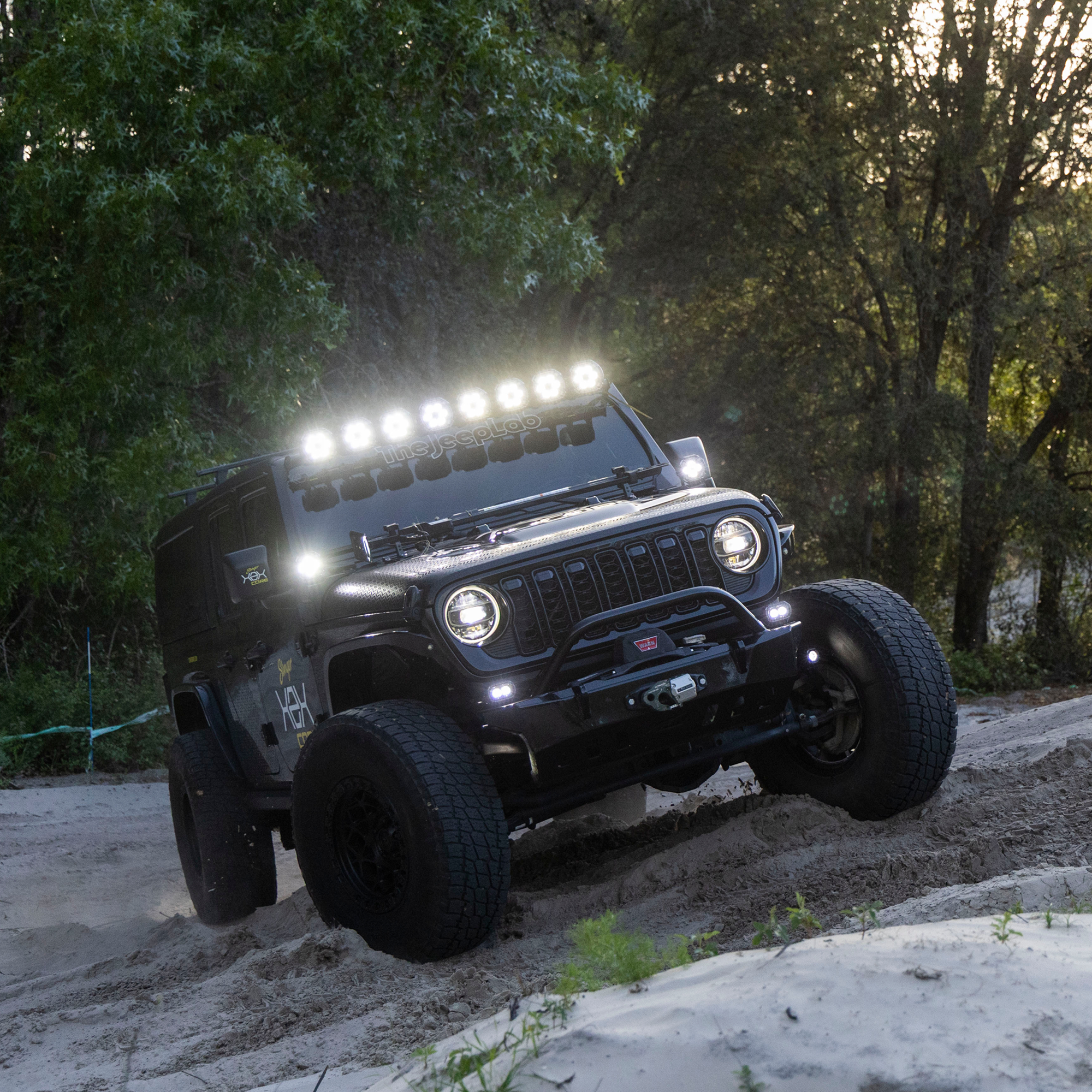 Black off-road Jeep with LED light bar driving on a sandy hill