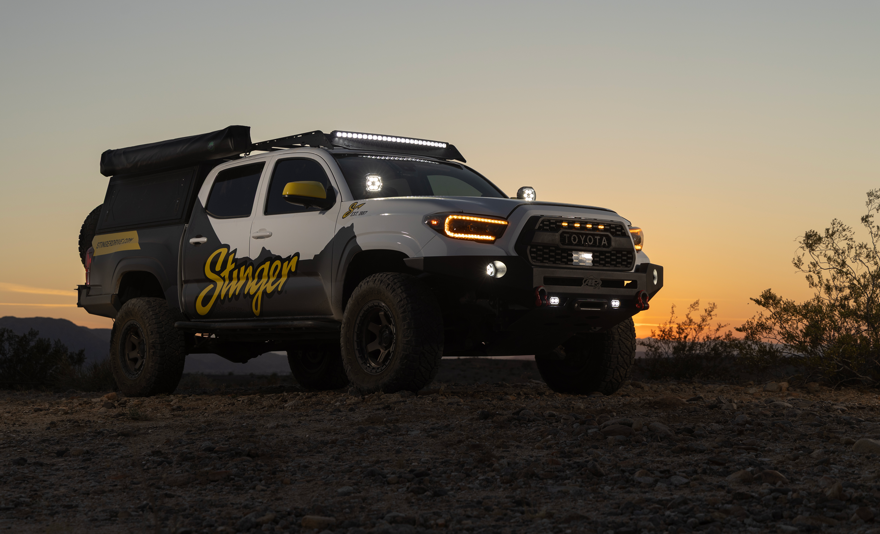 Off-road vehicle with 'Stinger' branding on a desert landscape at sunset.