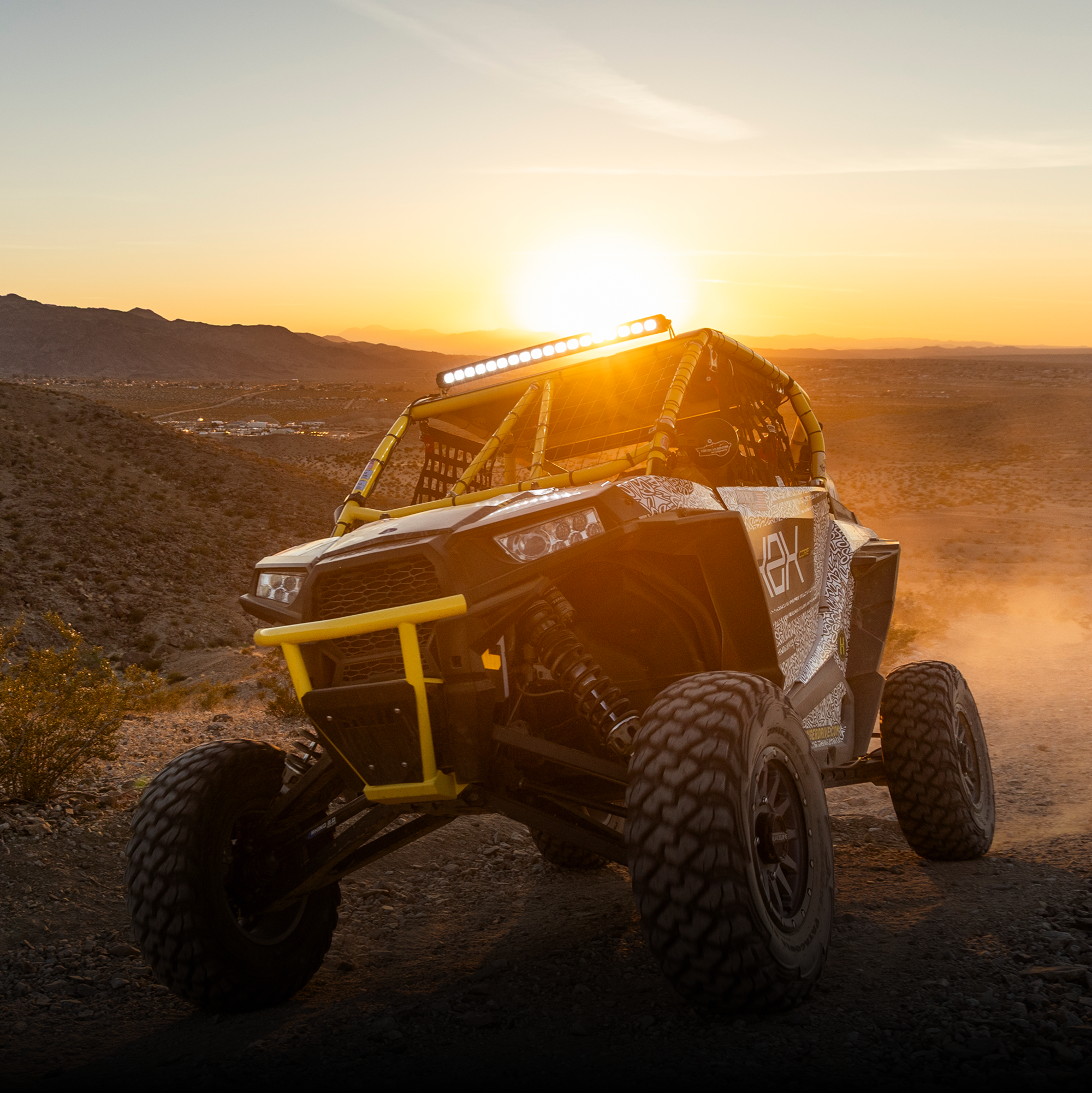 Off road vehicle with yellow roll cage parked on desert terrain at sunset