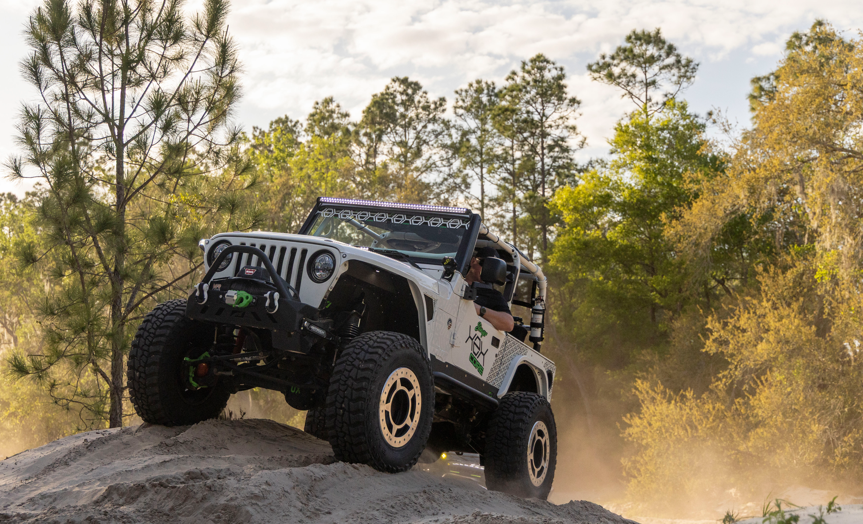 Jeep Wrangler driving on a dirt road with trees in the background