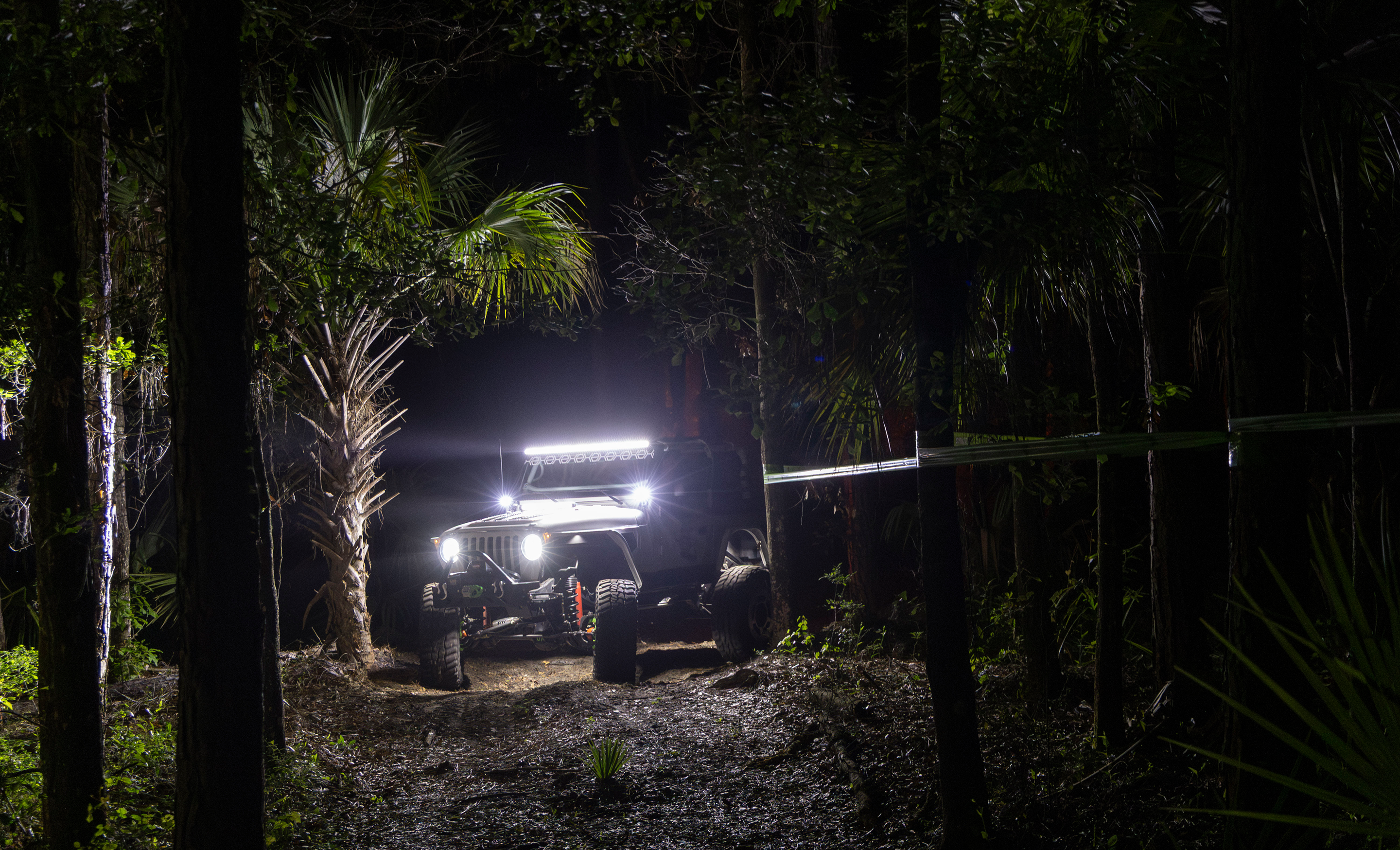Off-road vehicle with headlights on in a dark forest setting