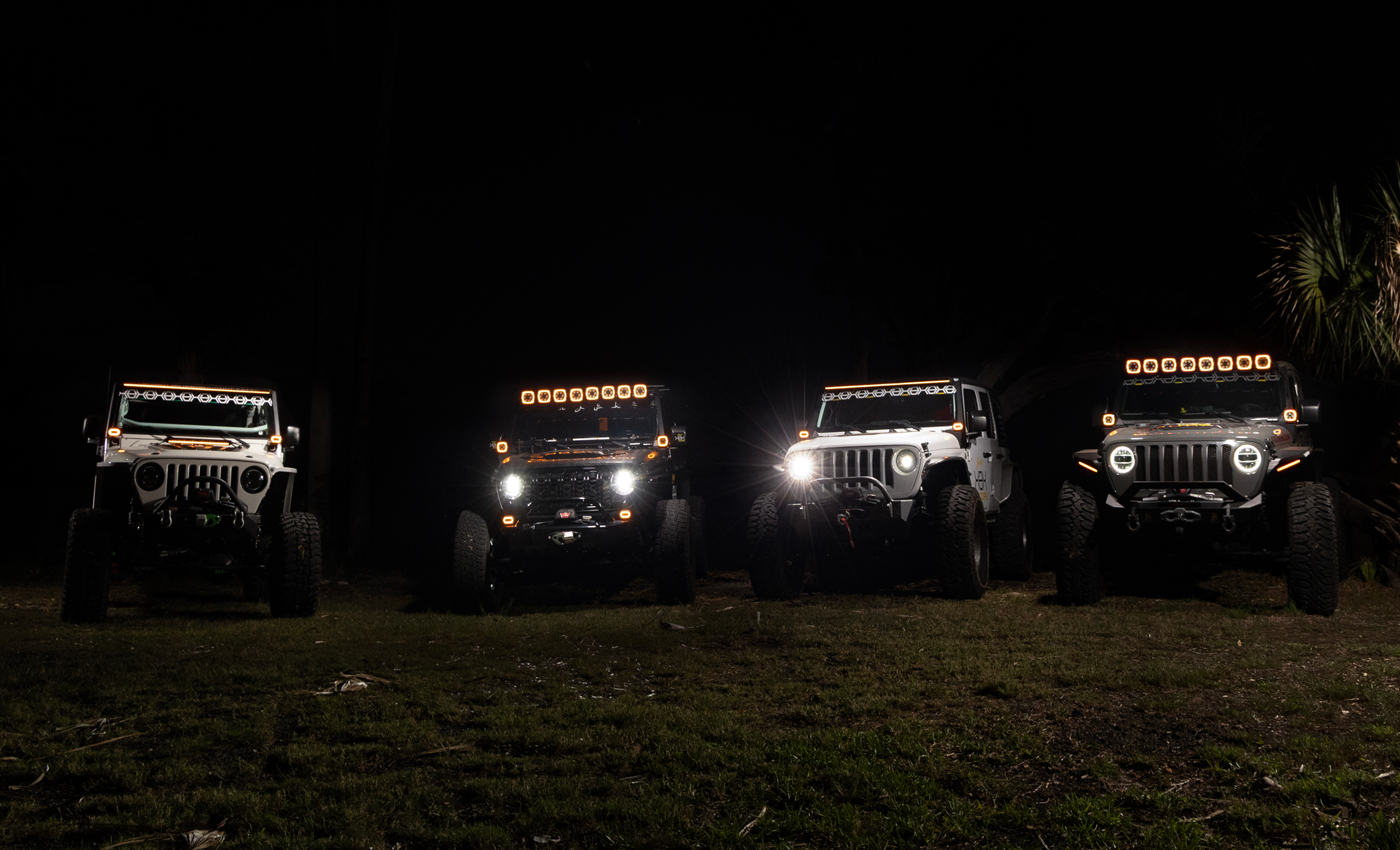 Four off-road vehicles with illuminated headlights on a dark background