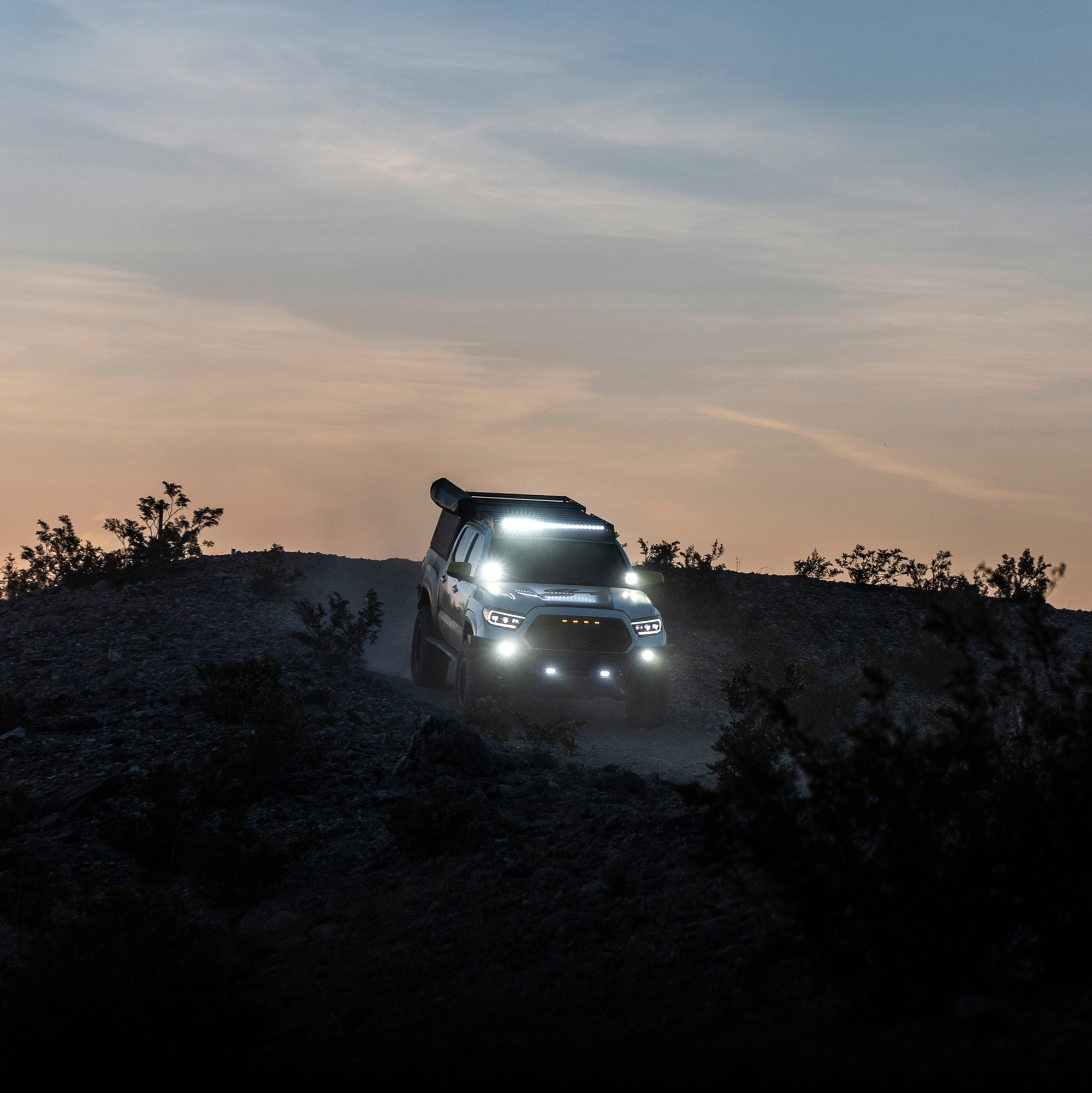Off-road vehicle driving on a dirt road at dusk with headlights on