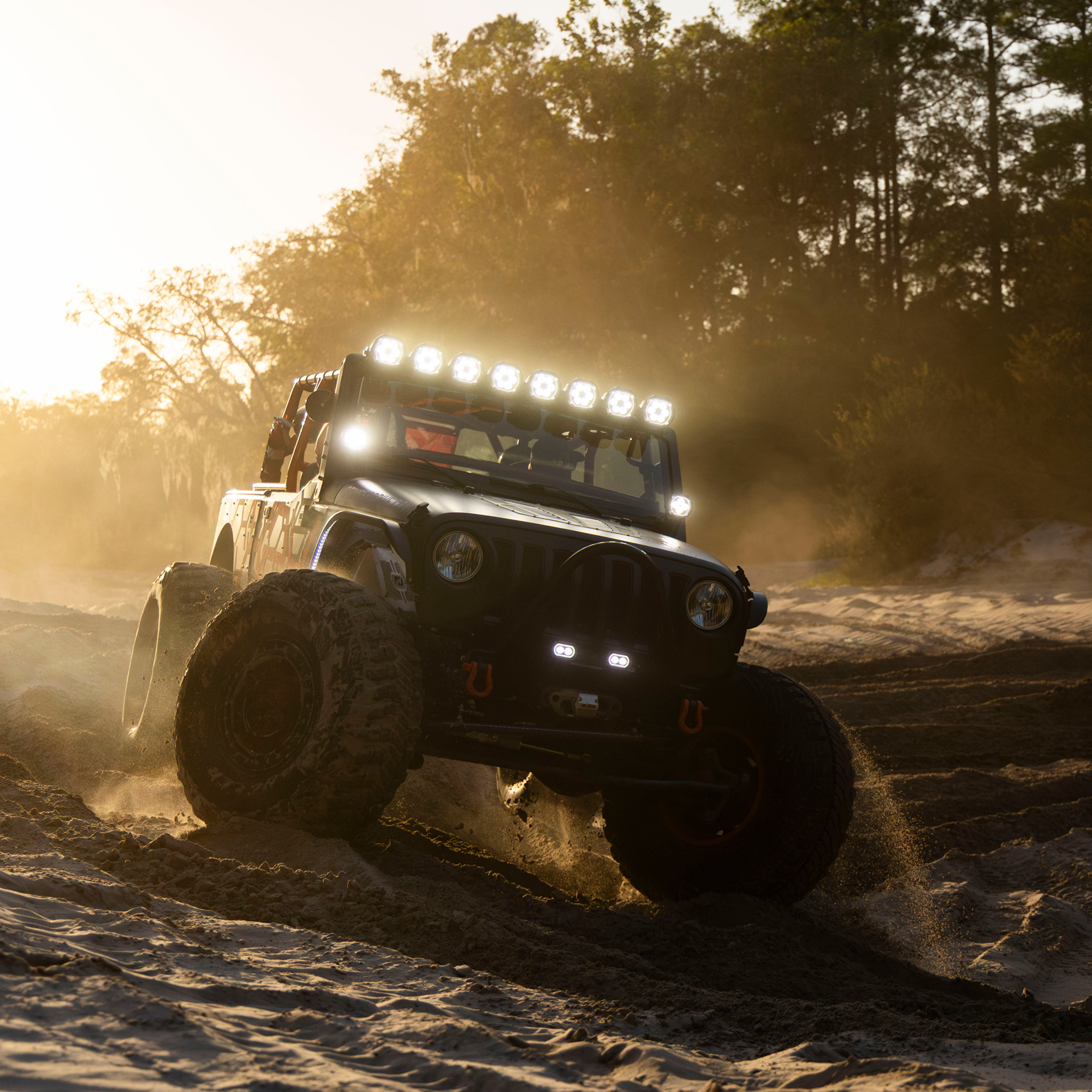 Modified off road vehicle driving through sand with roof mounted LED lights illuminated
