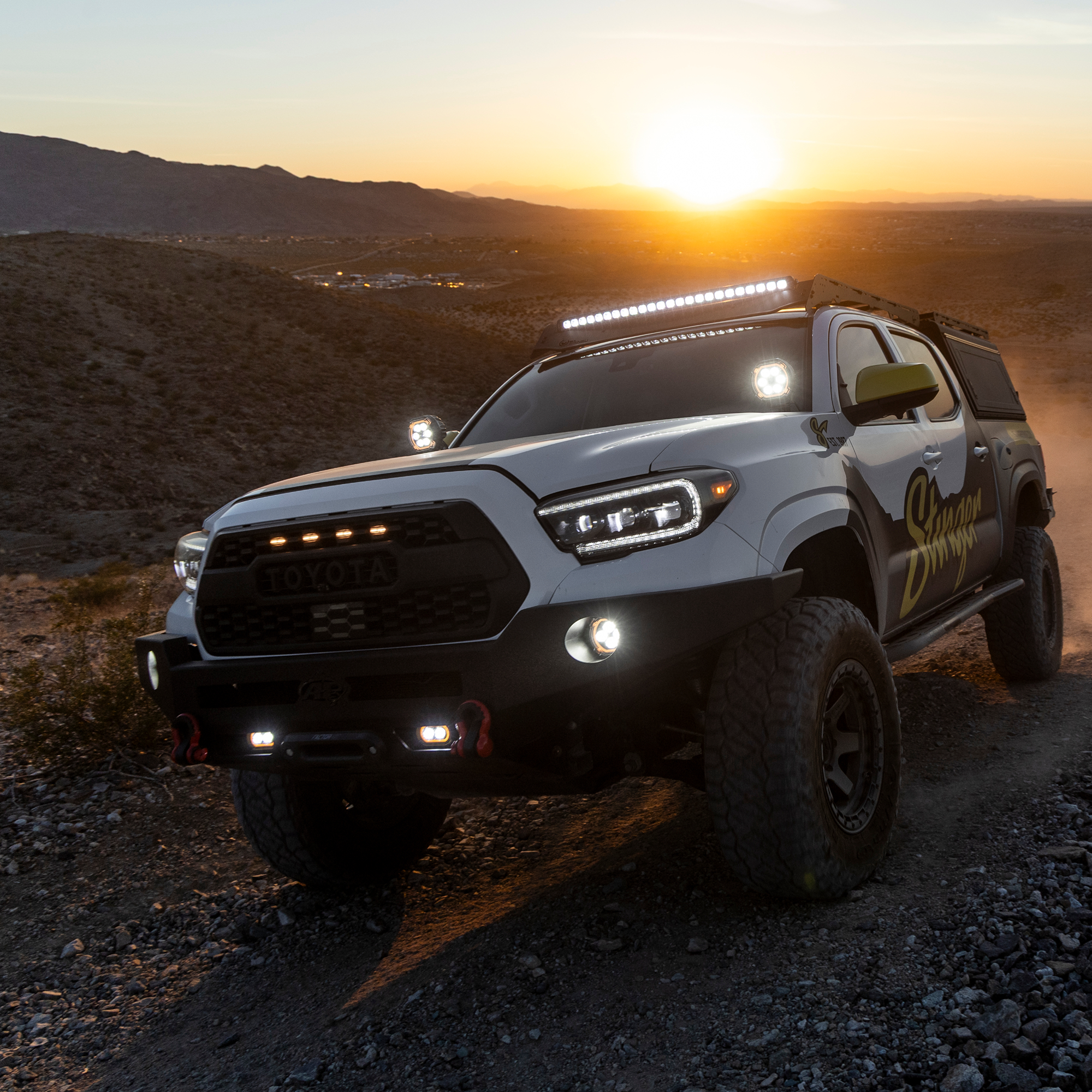 Modified white Toyota Tacoma truck driving on a desert trail at sunset