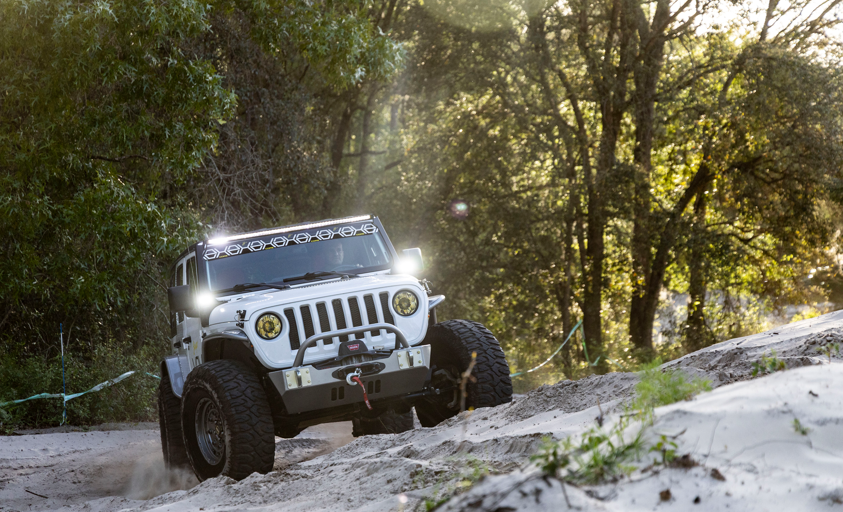 White off-road vehicle driving on a dirt path through a forest