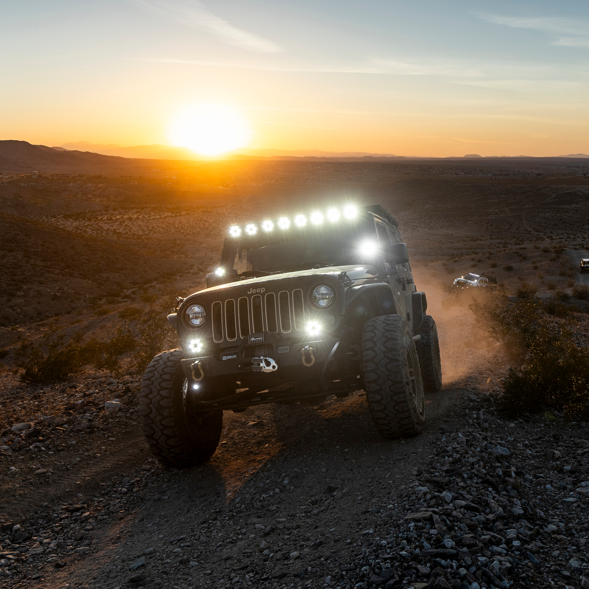 Jeep Wrangler driving on a rocky desert trail at sunset with LED light bar illuminated