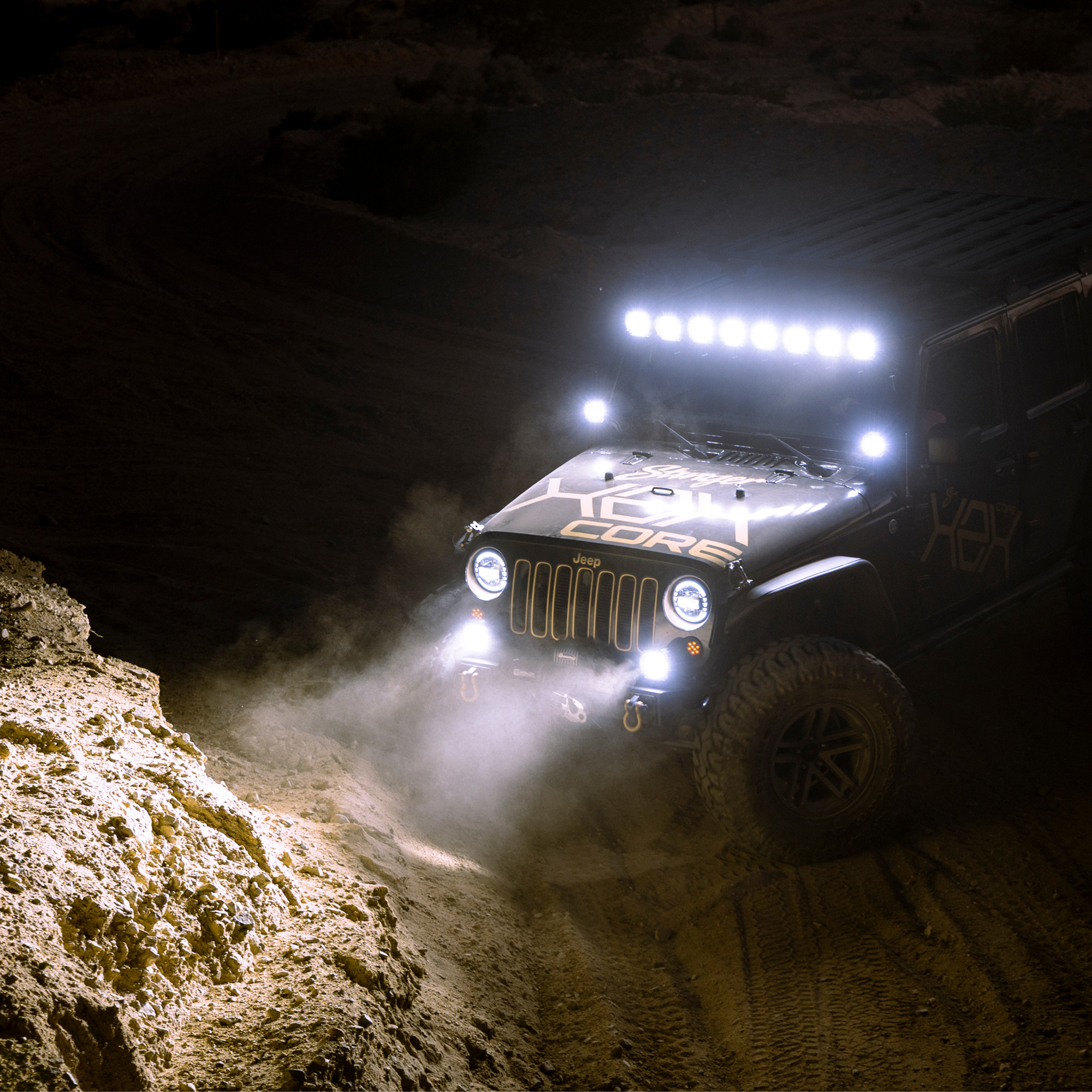Black Jeep with illuminated LED light bar and fog lights driving on a dark dirt trail
