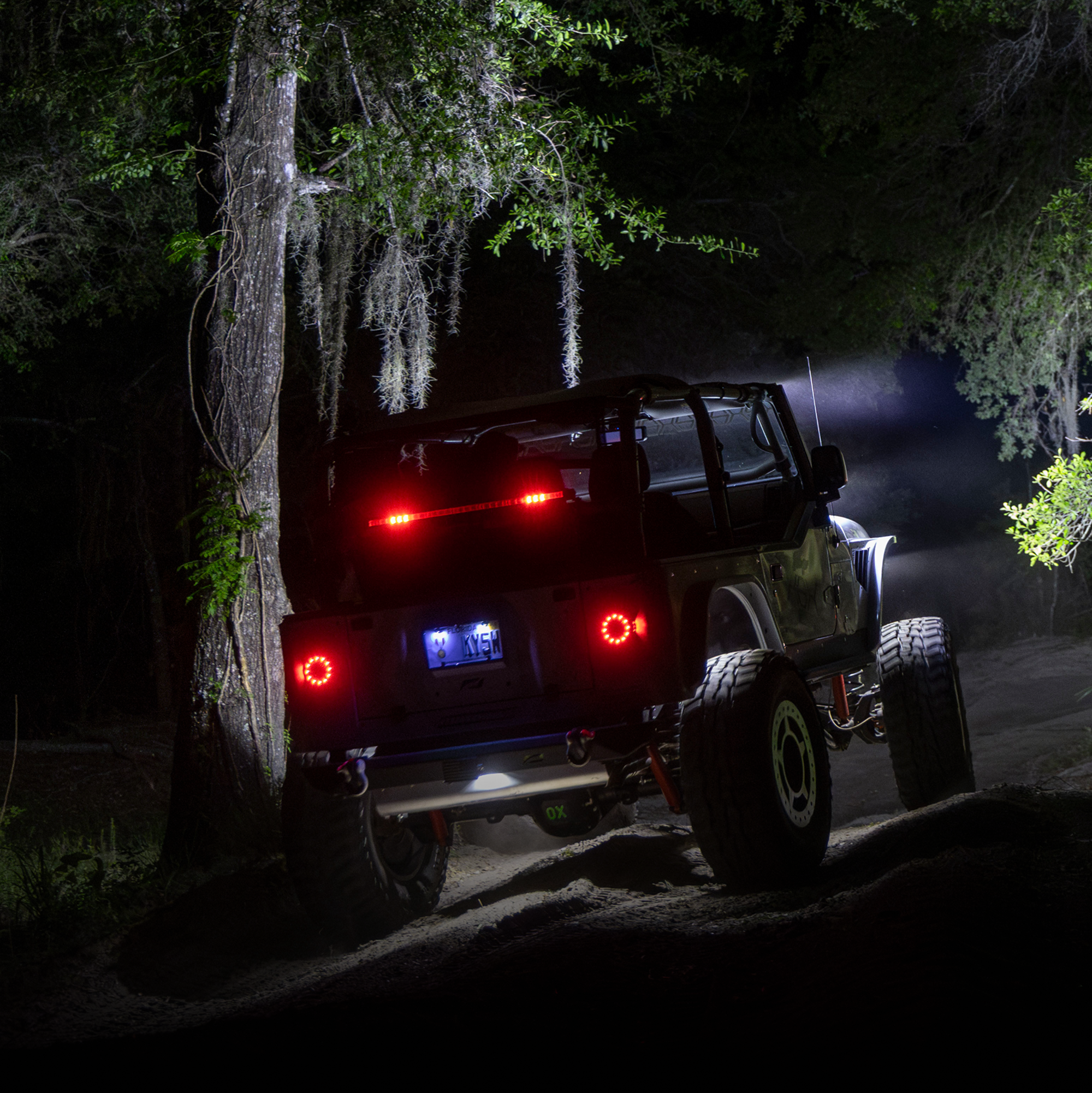 Off road vehicle with illuminated tail lights driving on a dark forest trail at night