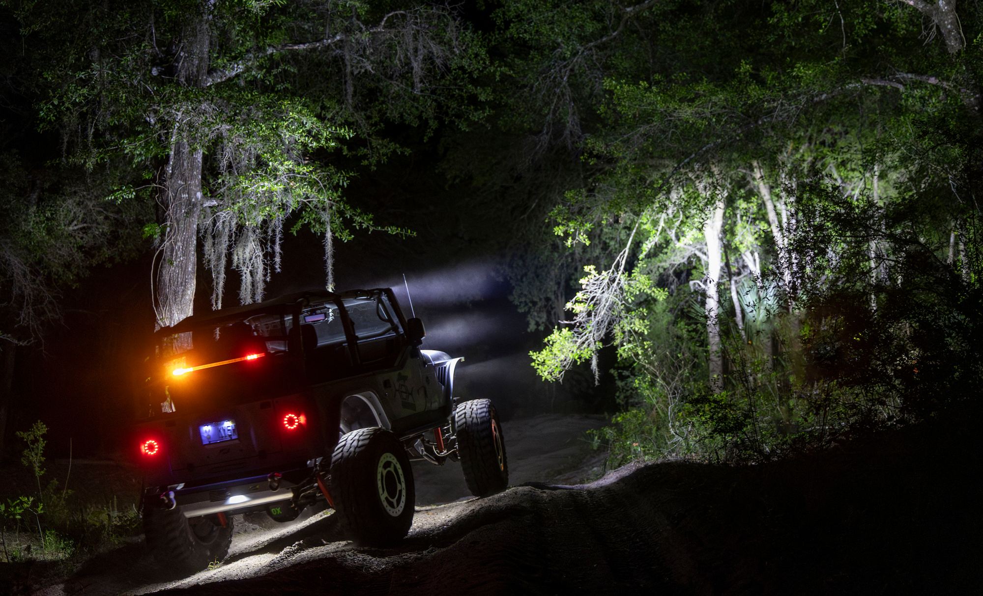 Jeep driving through a dark forest at night with lights on
