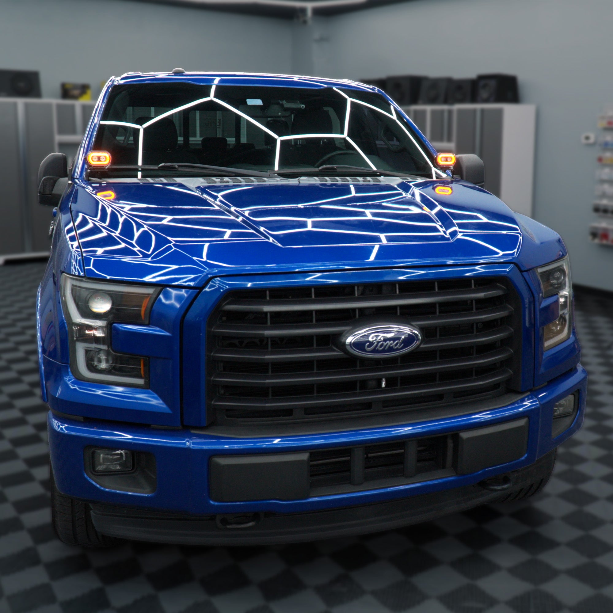 A bright blue Ford pickup truck photographed from the front in a garage or showroom with a black-and-white checkered floor and gray walls.