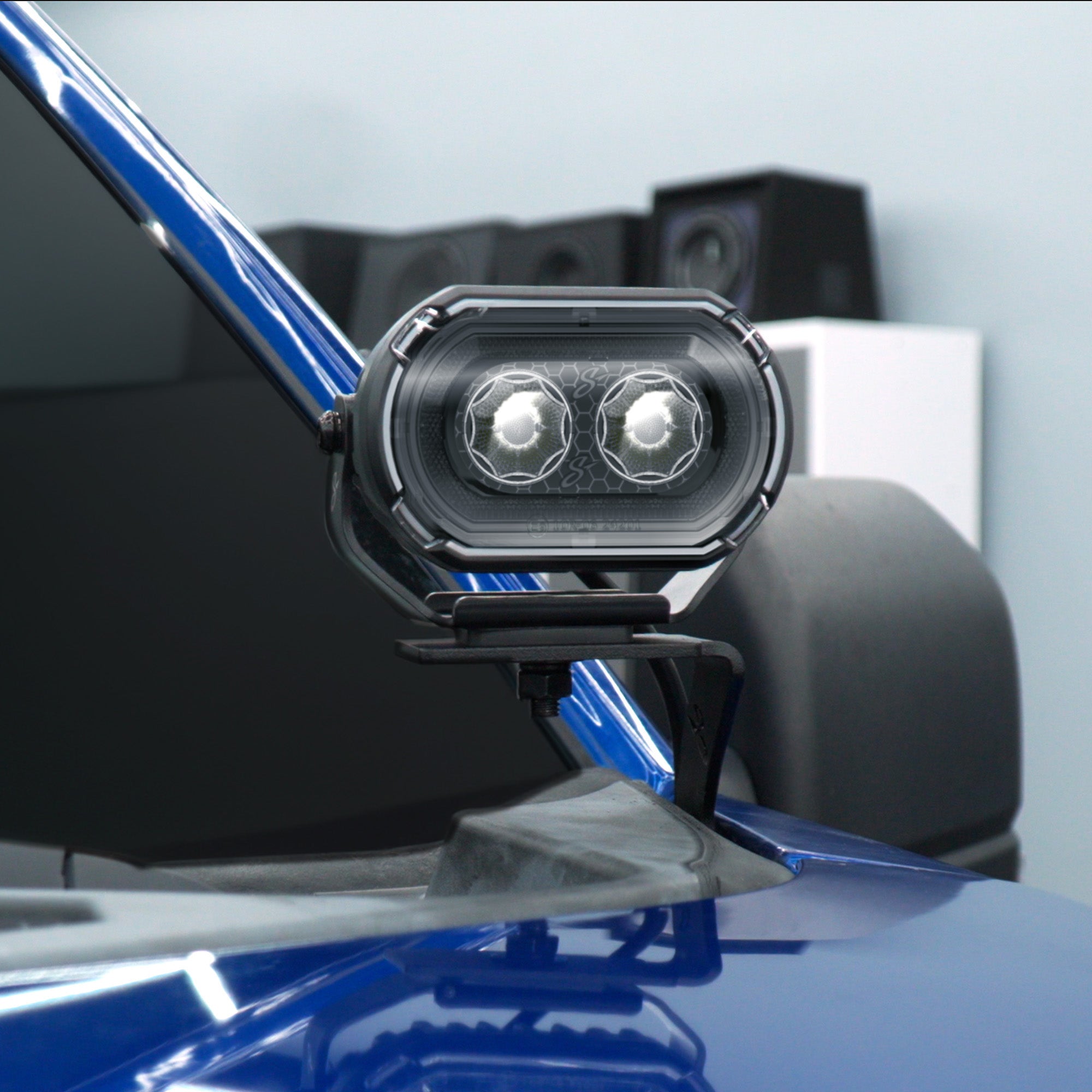 A black dual-light LED auxiliary vehicle light mounted on the side of a blue vehicle, shown in a clean, professional setting.