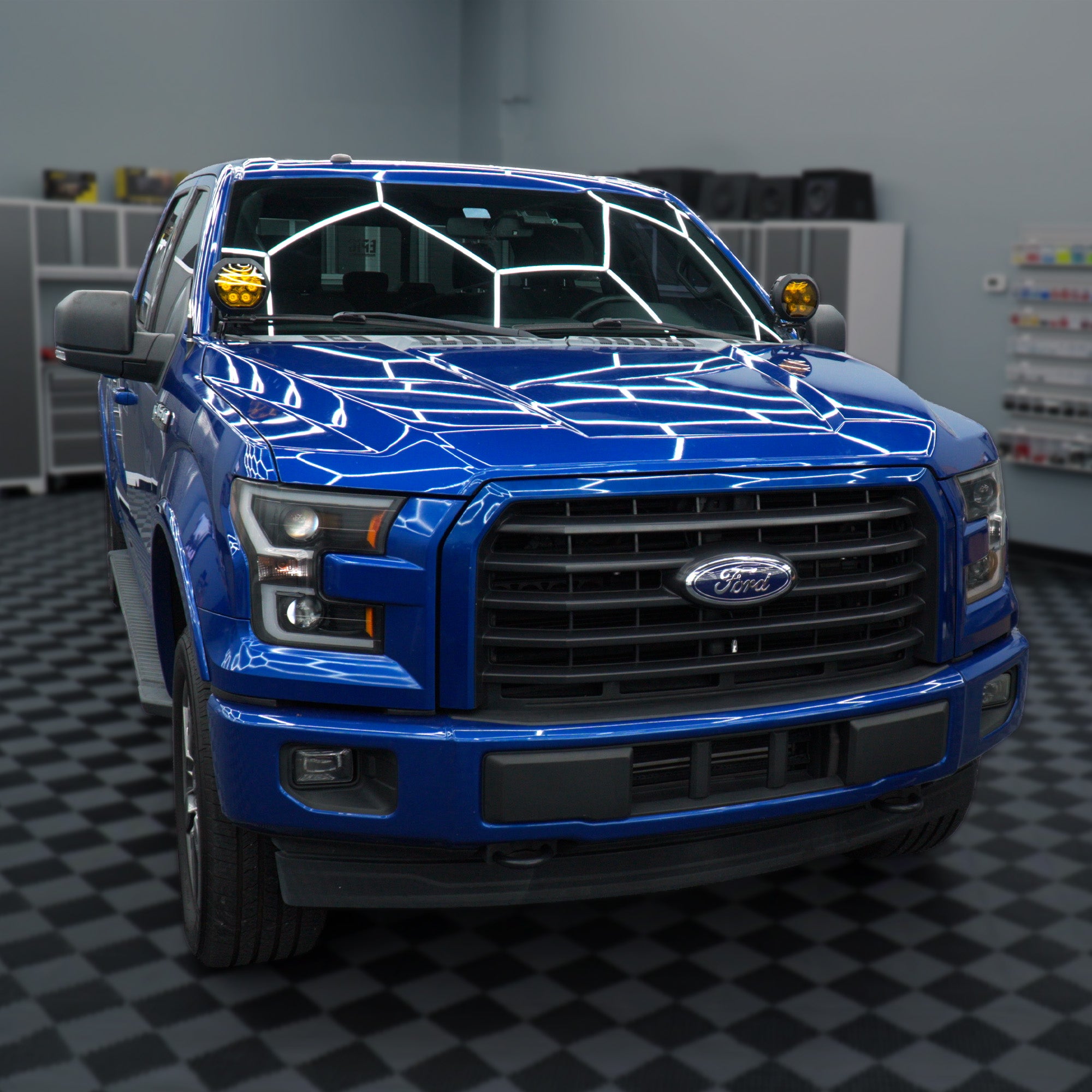 A bright blue Ford pickup truck photographed from the front in an indoor showroom or garage with a black-and-white checkered floor and gray walls.