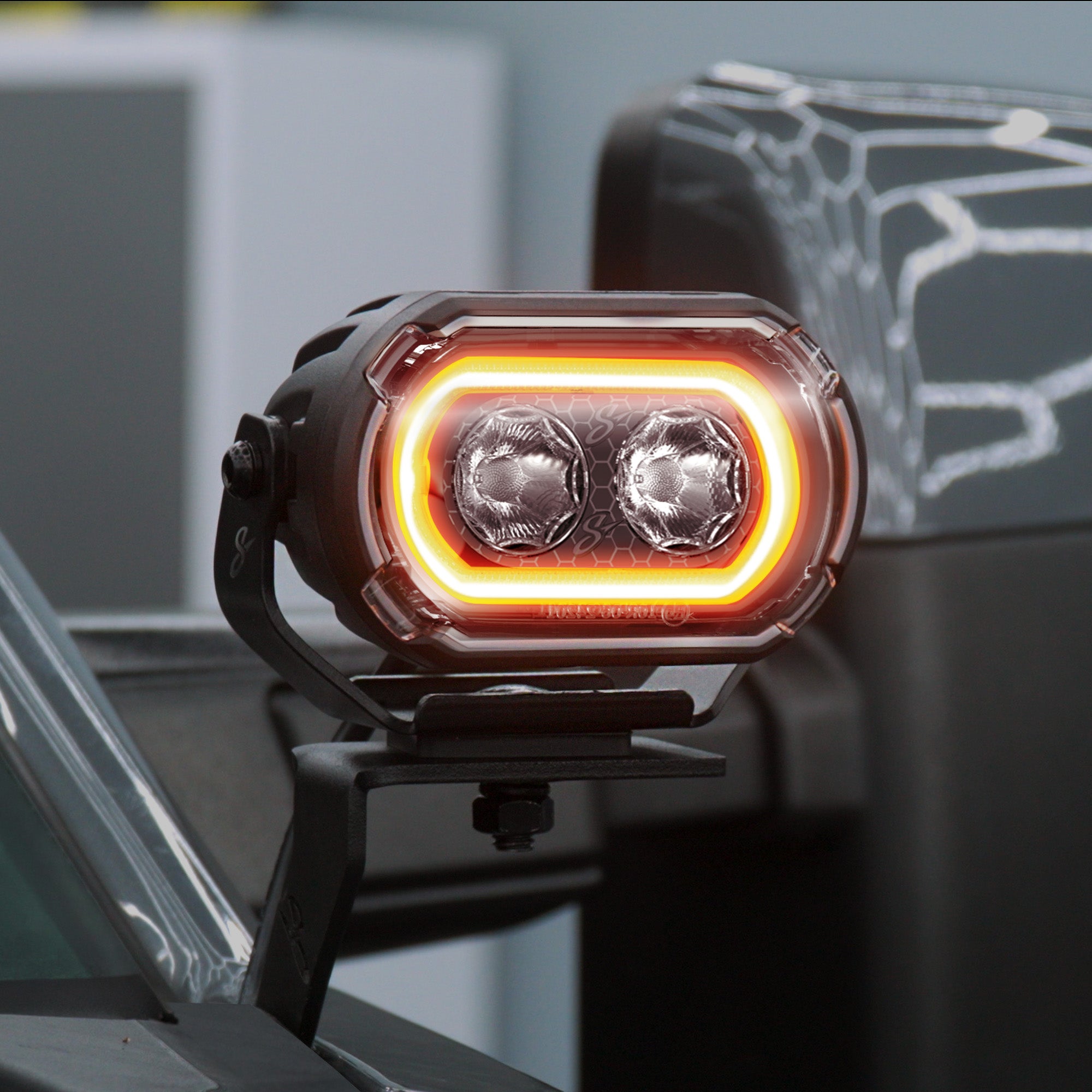 A close-up of a black car side marker light with dual LED bulbs and a glowing amber light bar, mounted on a vehicle side mirror.