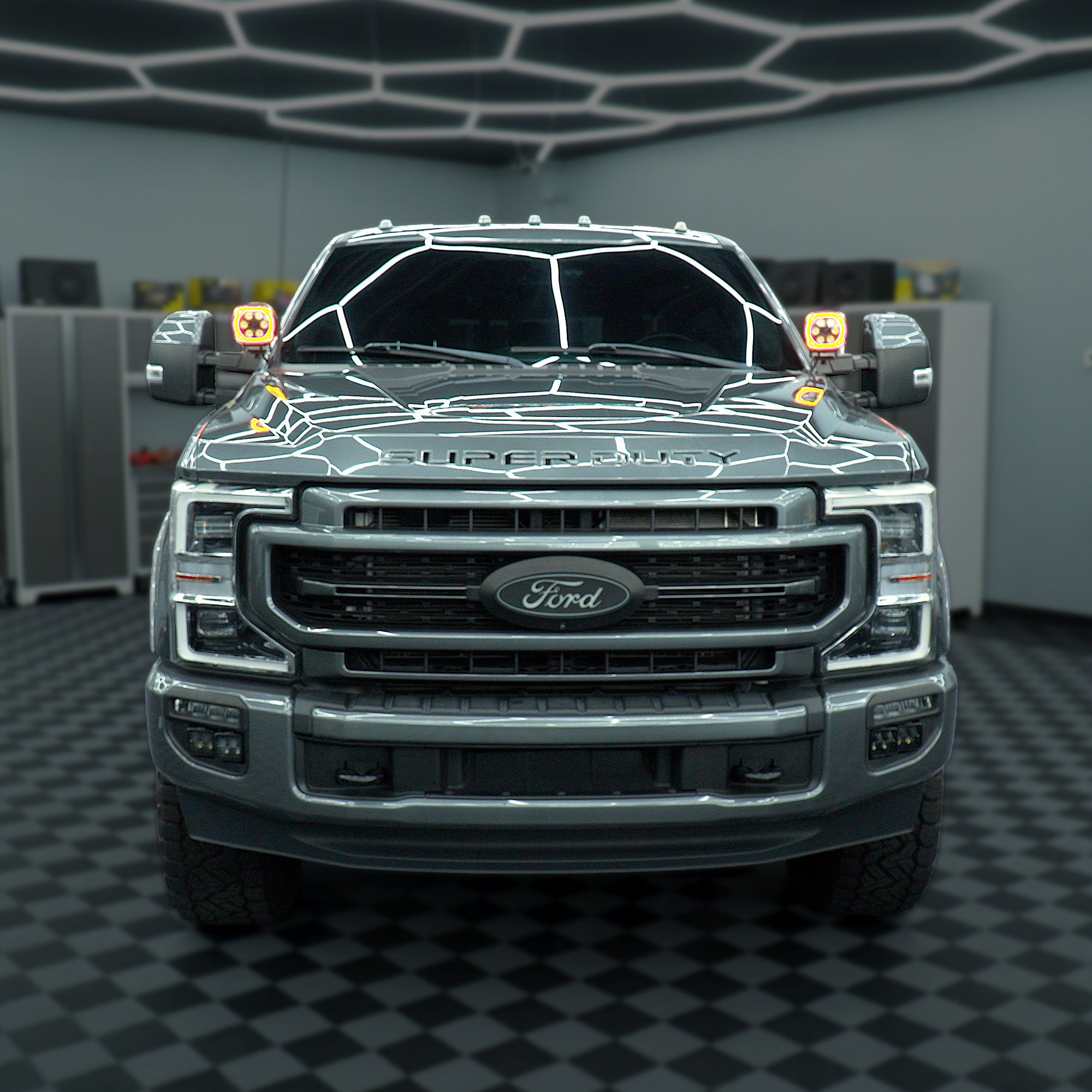 A dark gray Ford Super Duty pickup truck shown from the front in a garage setting with a black-and-white checkered floor and ceiling light fixtures.