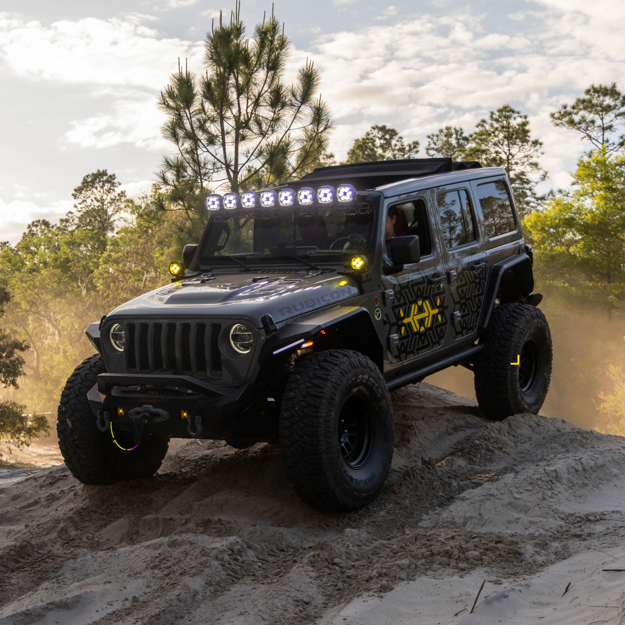 Grey Jeep Rubicon driving over a sand dune with LED roof lights on