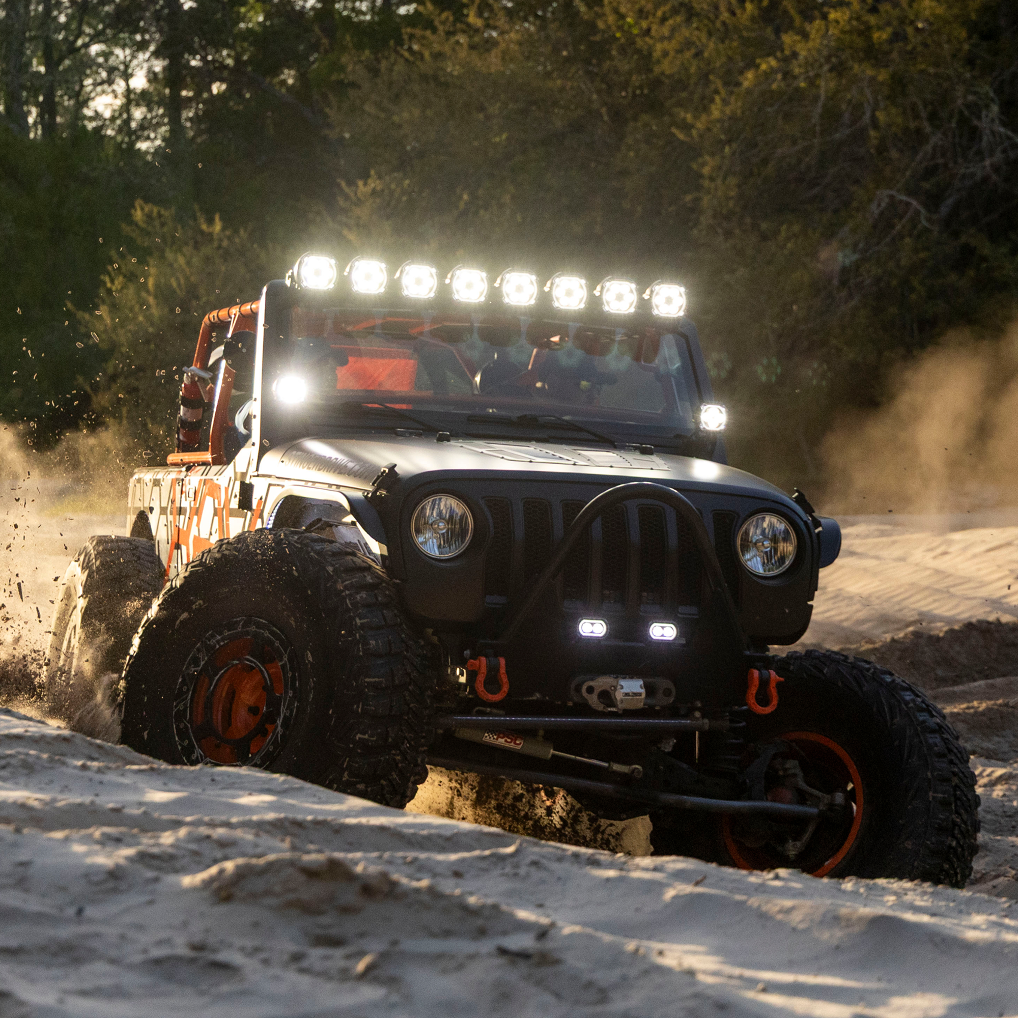 Black off road vehicle with bright roof lights driving through sand