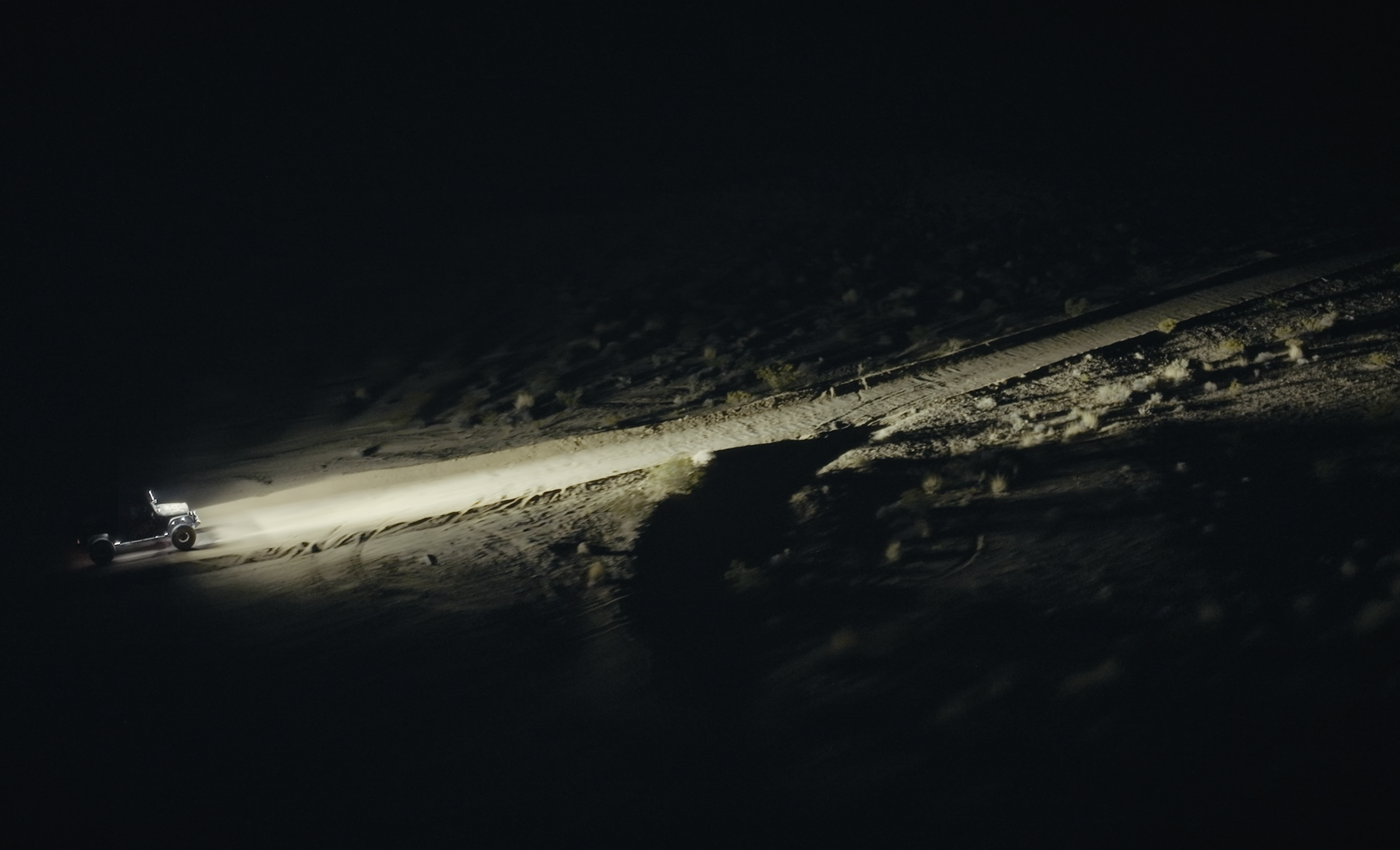 Off road vehicle driving on desert terrain at night with headlights illuminating the path