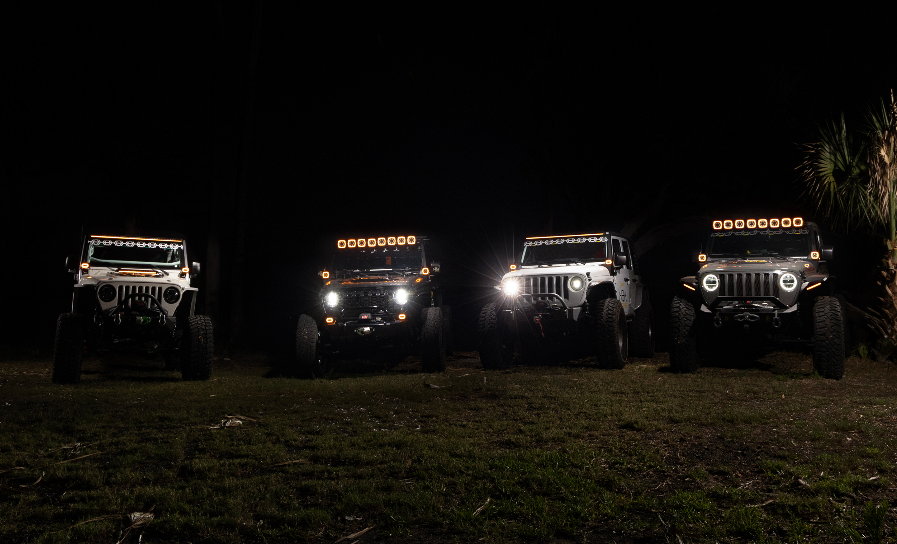 Four off-road vehicles parked in a row at night with illuminated headlights and roof lights