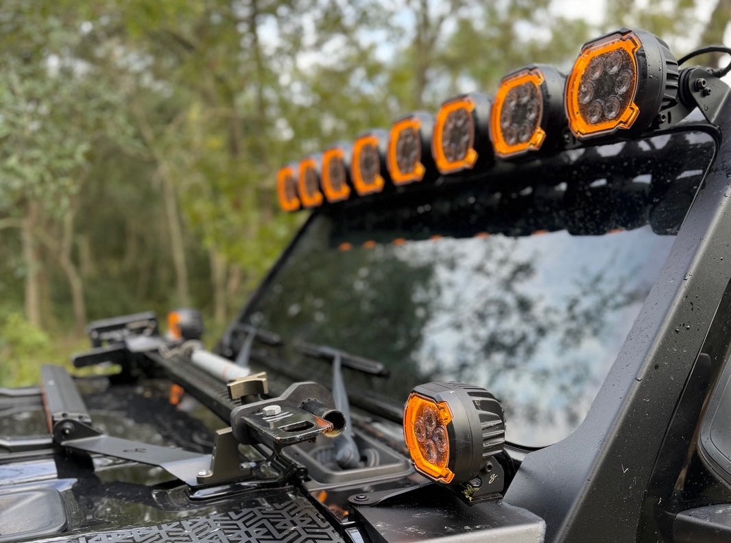 Off-road vehicle equipped with a roof-mounted LED light bar and two orange accent side lights, photographed outdoors with trees in the background.