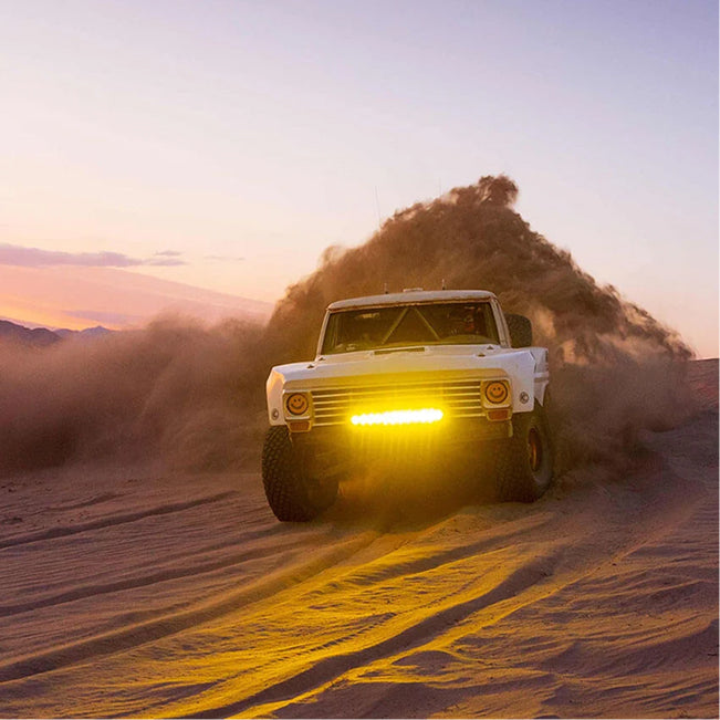 White off road truck driving through sand dunes with bright yellow LED light bar illuminated