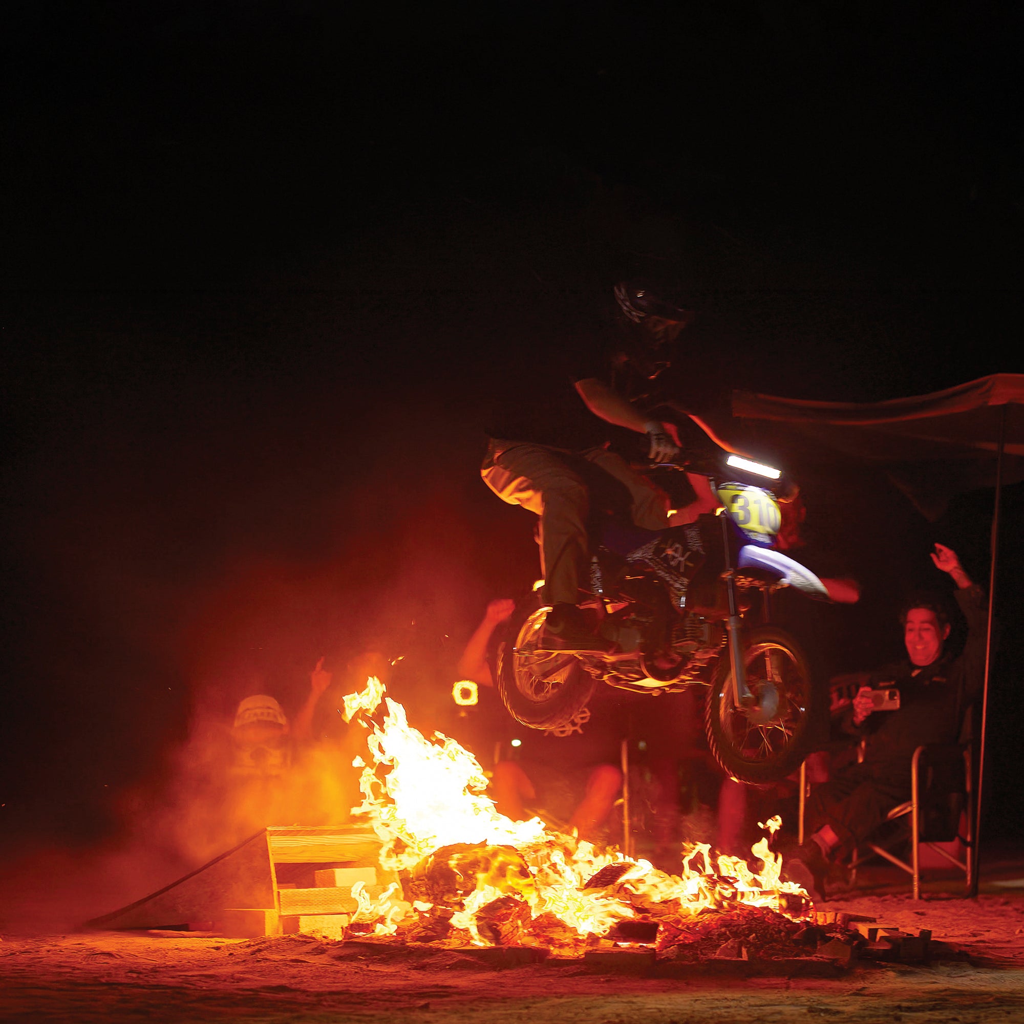 Person on a motorcycle performing a stunt over flames at night