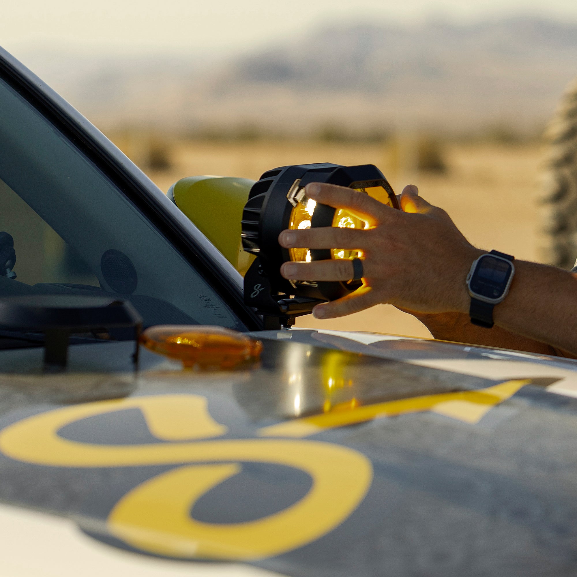 Hand adjusting a circular yellow off-road light mounted on a vehicle hood
