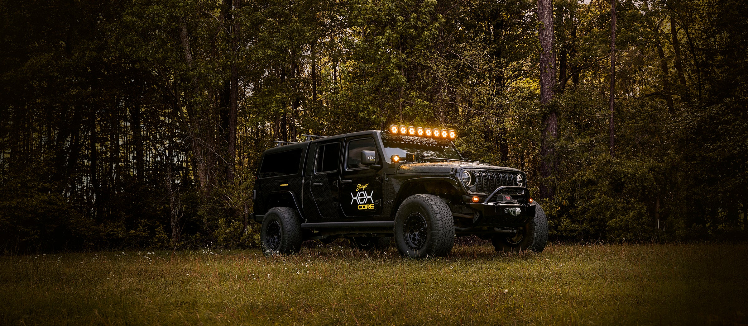 Black off-road vehicle with illuminated roof lights in a forest setting
