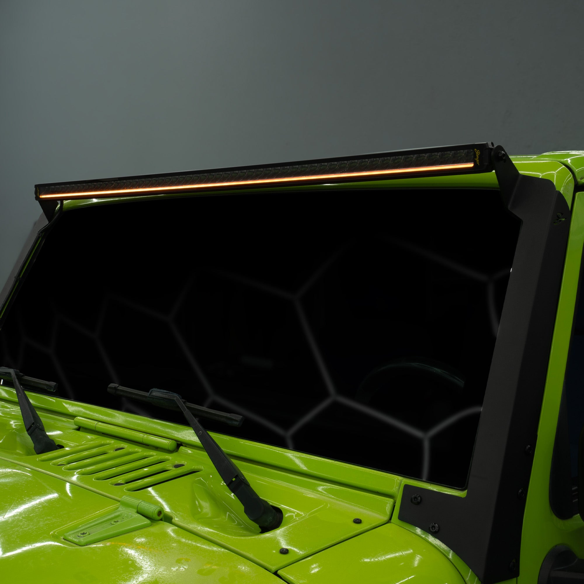 A close-up of a bright lime green vehicle with a black roof-mounted LED light bar illuminated above the dark tinted windshield.