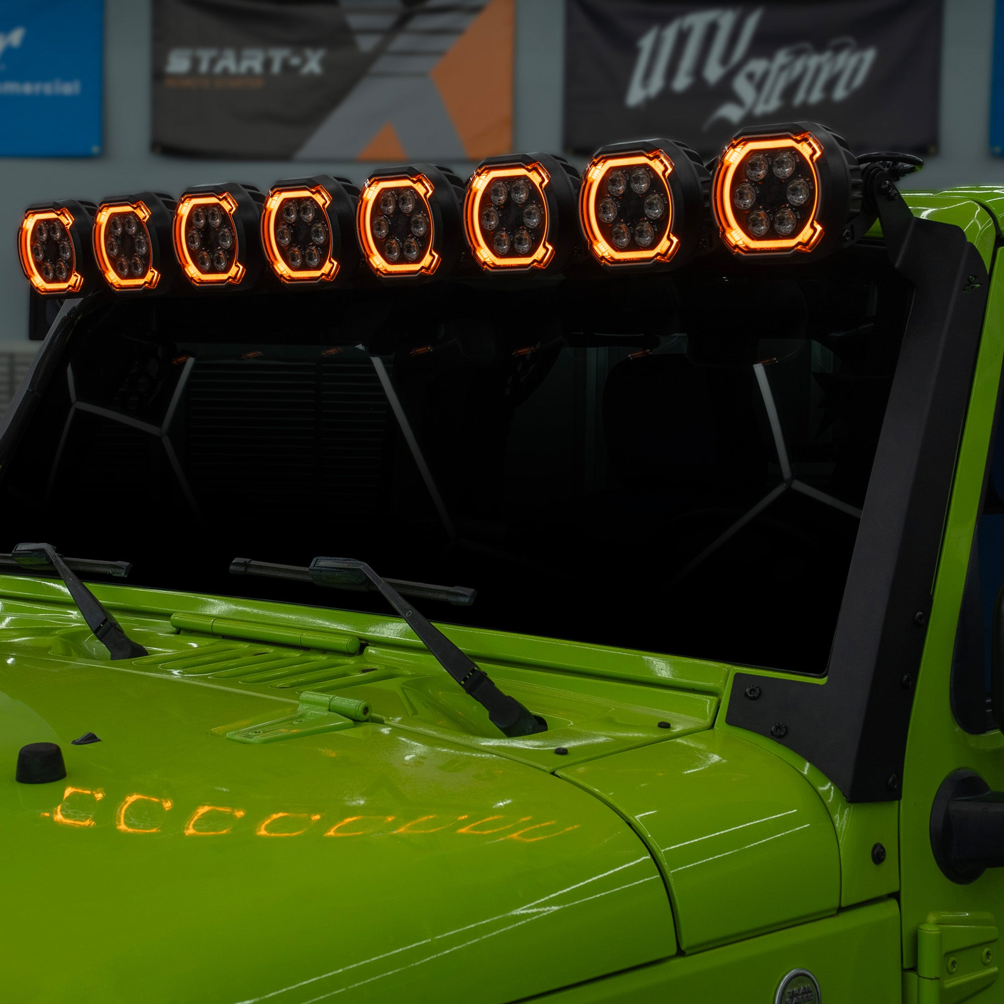 A row of eight bright LED off-road light bars mounted above the windshield of a lime green vehicle, with amber lights illuminated.