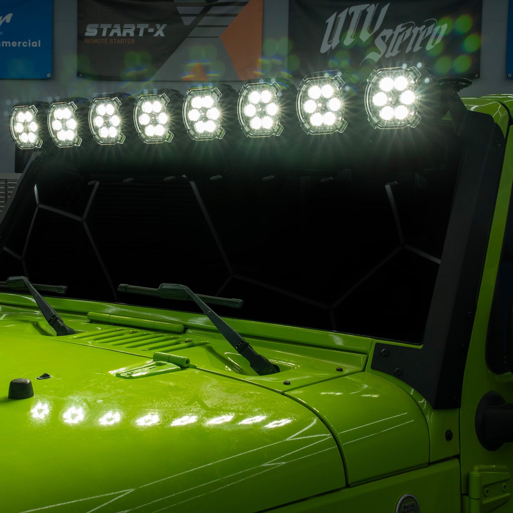 A row of eight bright LED off-road light bars mounted above the windshield of a lime green vehicle, photographed in a showroom or garage setting.