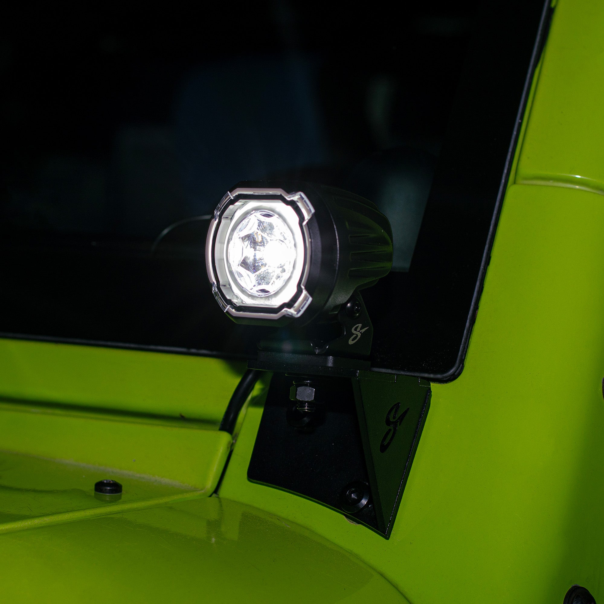 A compact LED off-road light mounted on the side of a bright lime green vehicle, shown illuminated against a dark background.