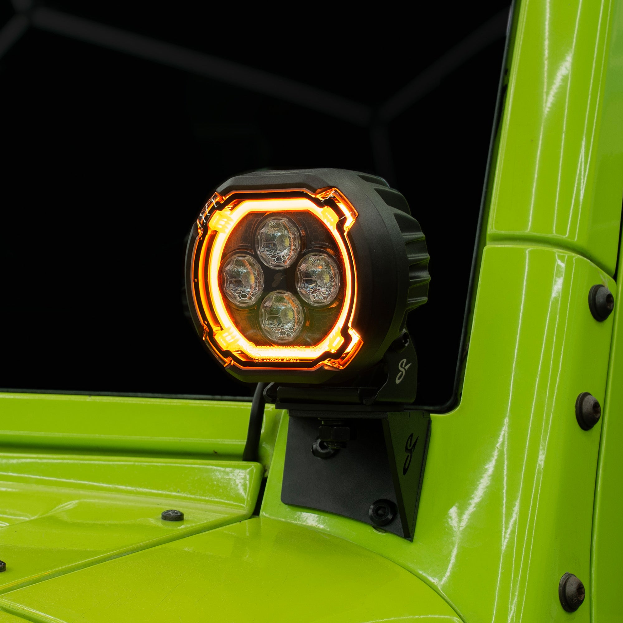 A close-up of a black off-road LED light mounted on the side of a bright lime green vehicle, with the light's amber and white light bars illuminated.