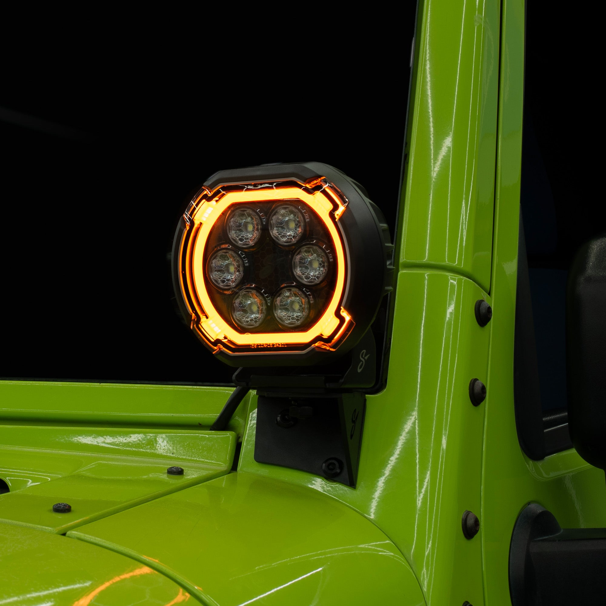 A close-up of a black off-road LED light mounted on the side of a bright lime green vehicle, with the light illuminated in amber.