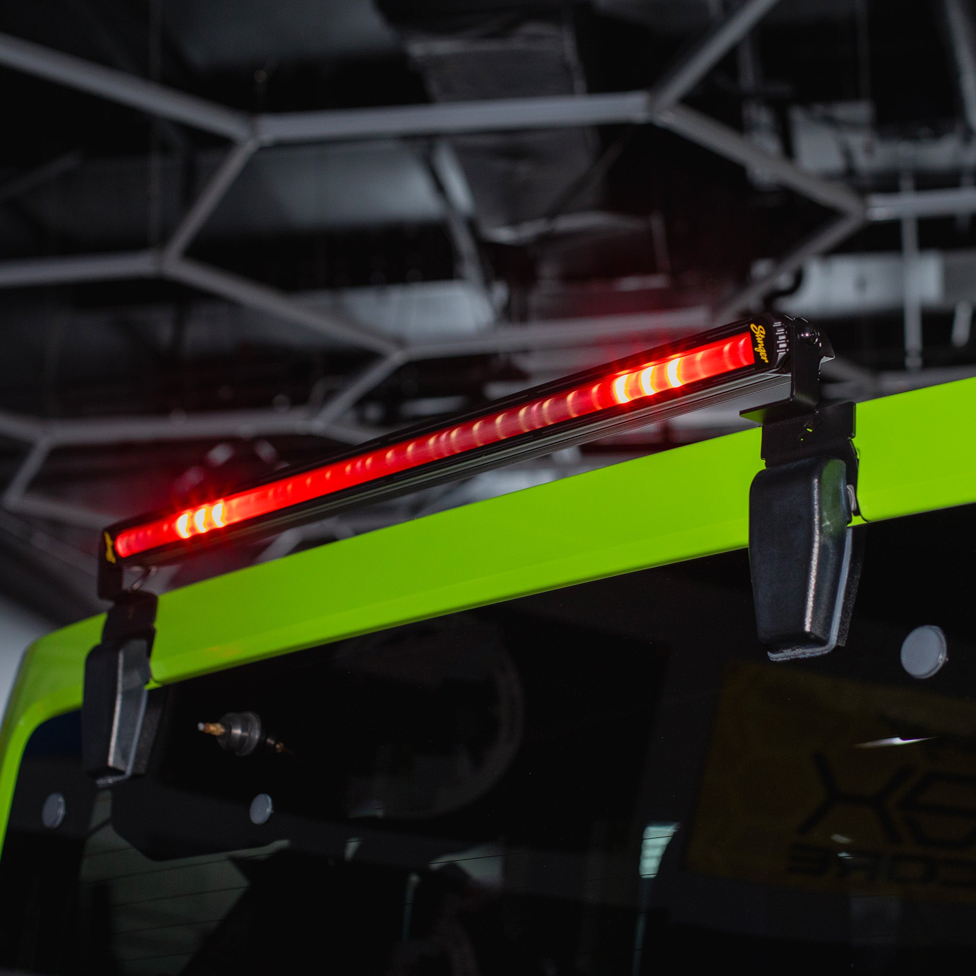 A bright red LED roof-mounted light bar clipped onto a high-visibility neon green vehicle roof rack, shown in a dark industrial setting.