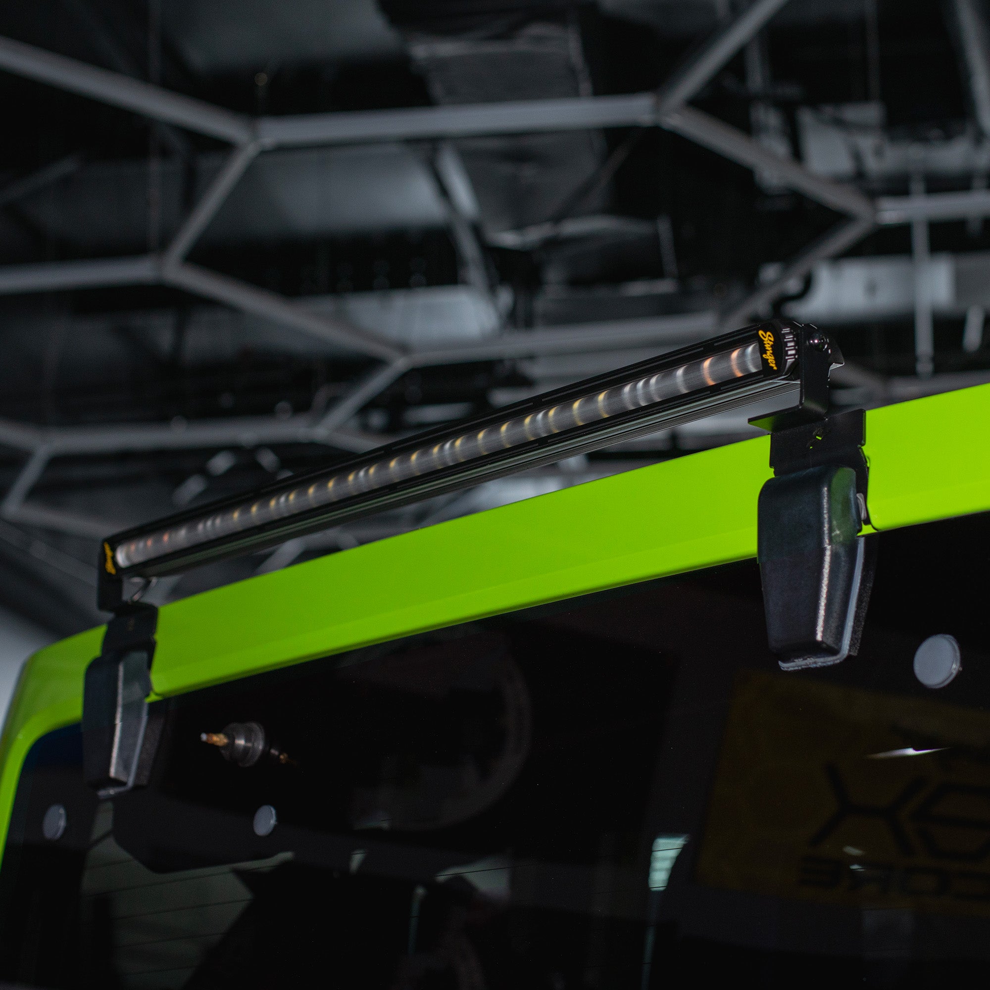 A long LED roof bar light mounted on the bright neon green roof of a vehicle, photographed in a dark industrial or garage setting.