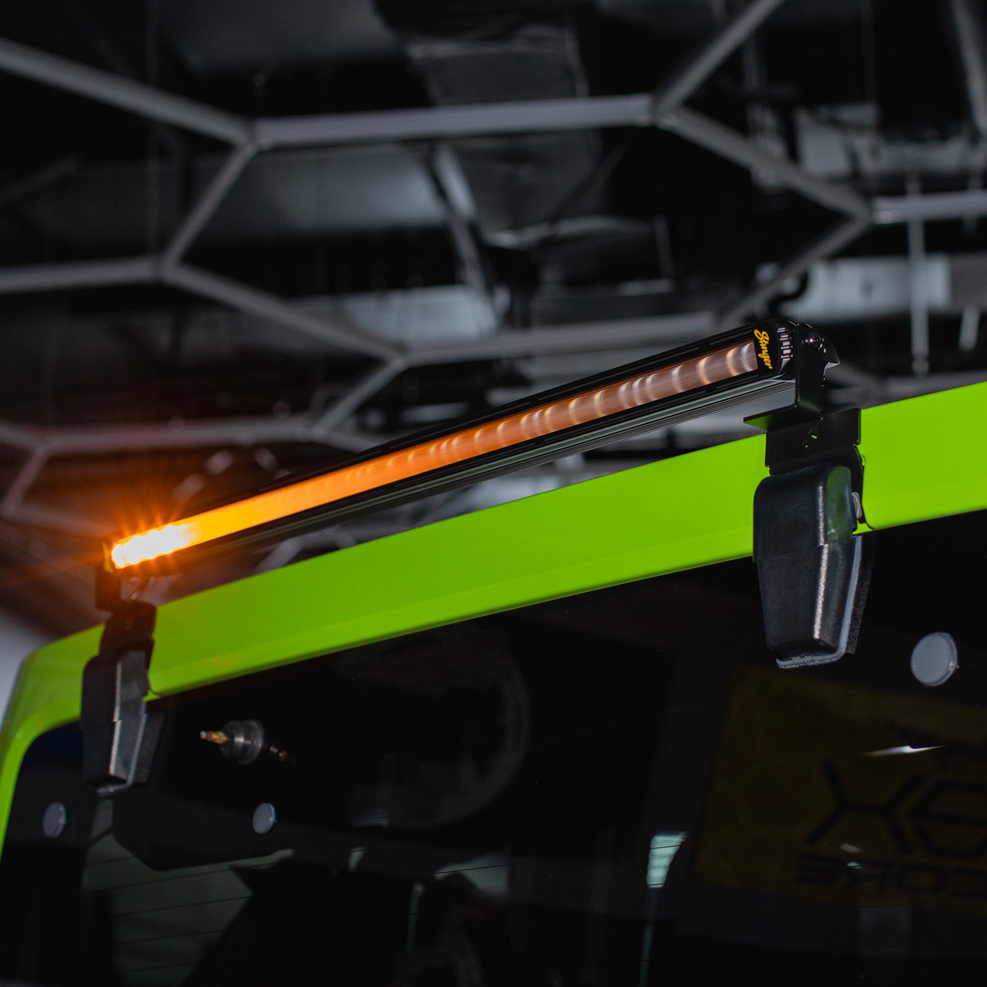 A long rectangular LED light bar with amber and white illumination, mounted on a bright neon green vehicle frame in a dark industrial setting.