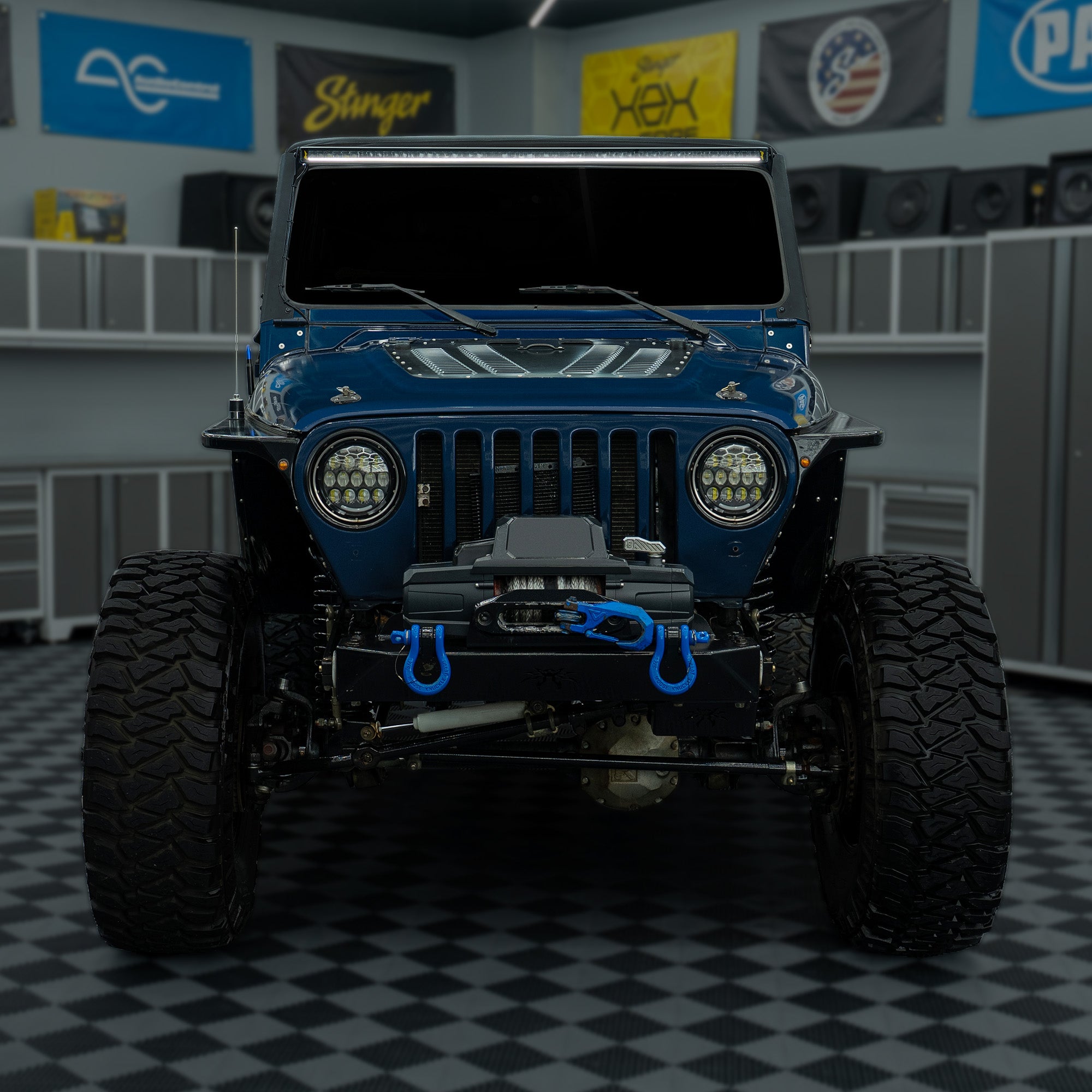 Front view of a blue Stinger Jeep with off-road tires and winch in a garage