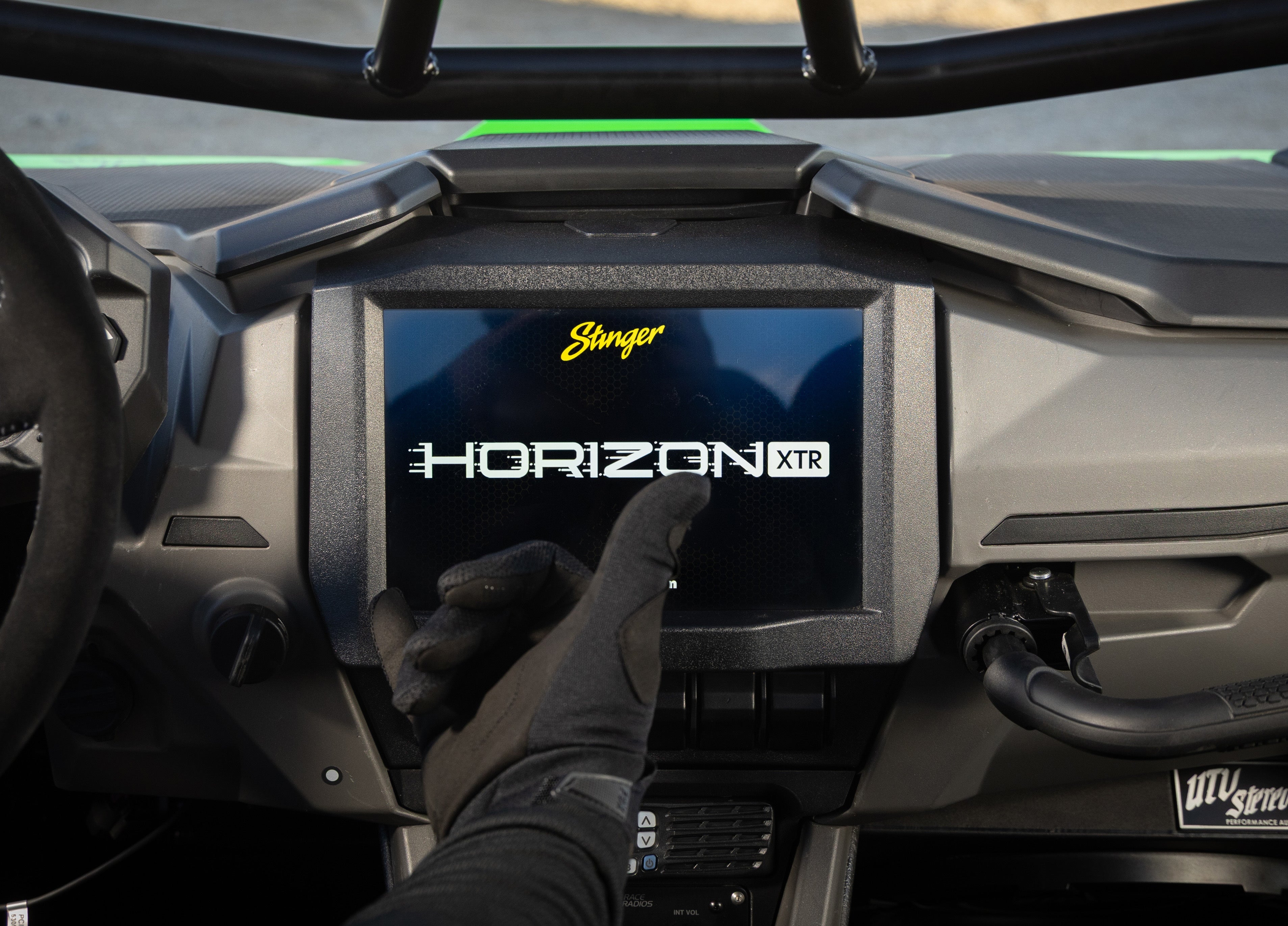 Gloved hand touching Stinger Horizon XTR infotainment screen in UTV dashboard