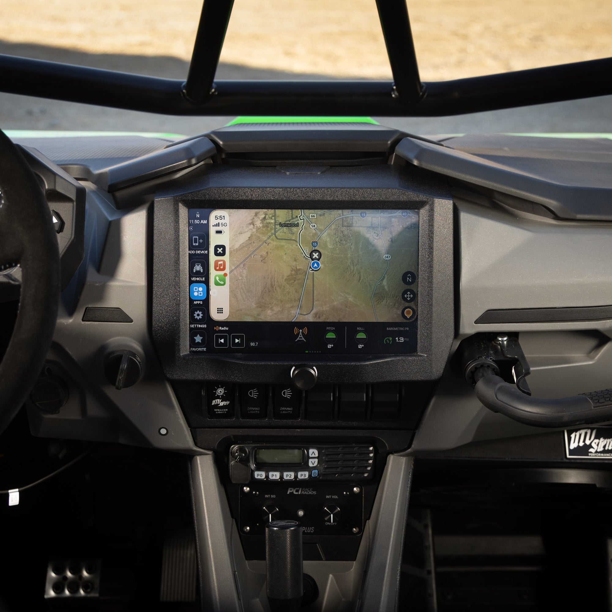 A close-up view of a vehicle's dashboard interior, centered on a large touchscreen display showing a navigation map. The cabin features a gray and black textured dashboard, a steering wheel on the left, and a gear shifter in the center.