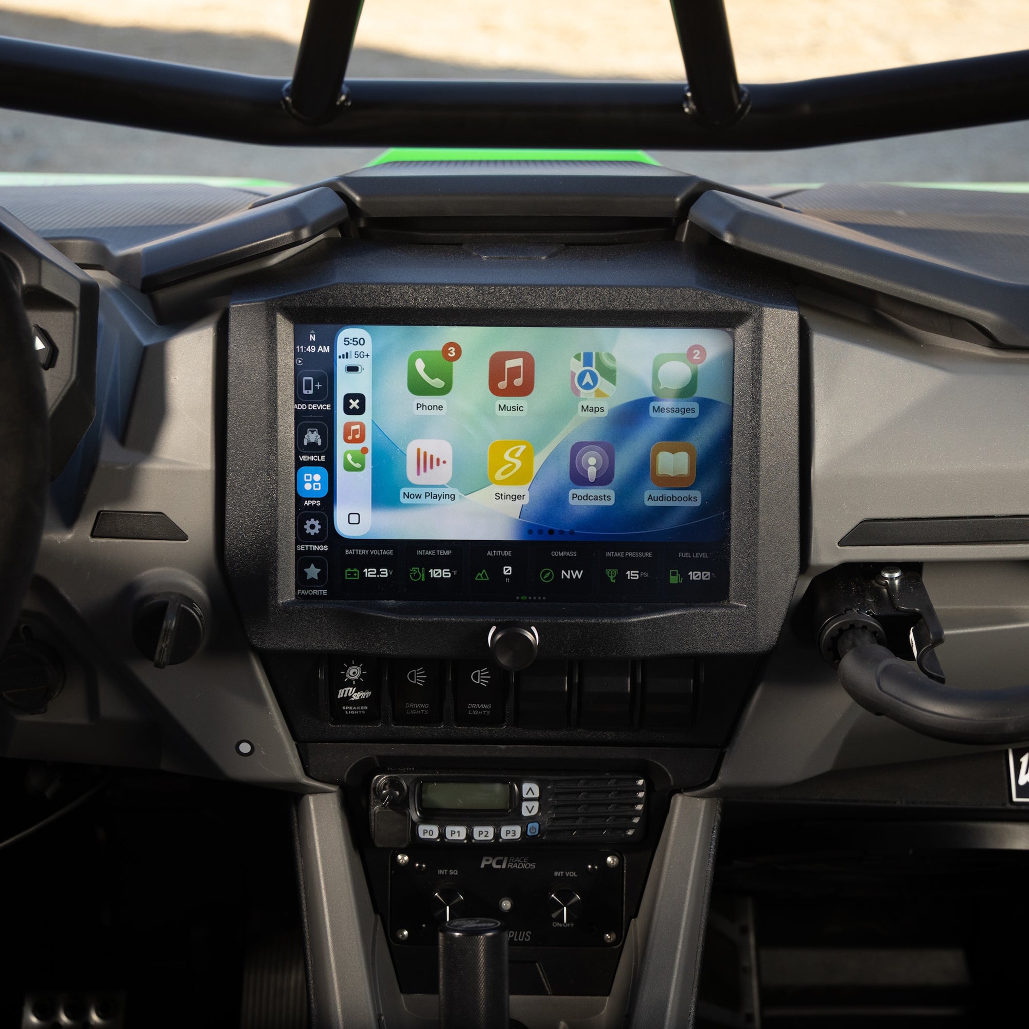 A large touchscreen infotainment system mounted in the center console of a vehicle dashboard, displaying Apple CarPlay interface apps. Below the screen are physical controls and a lower display, with the gear shift selector visible below.