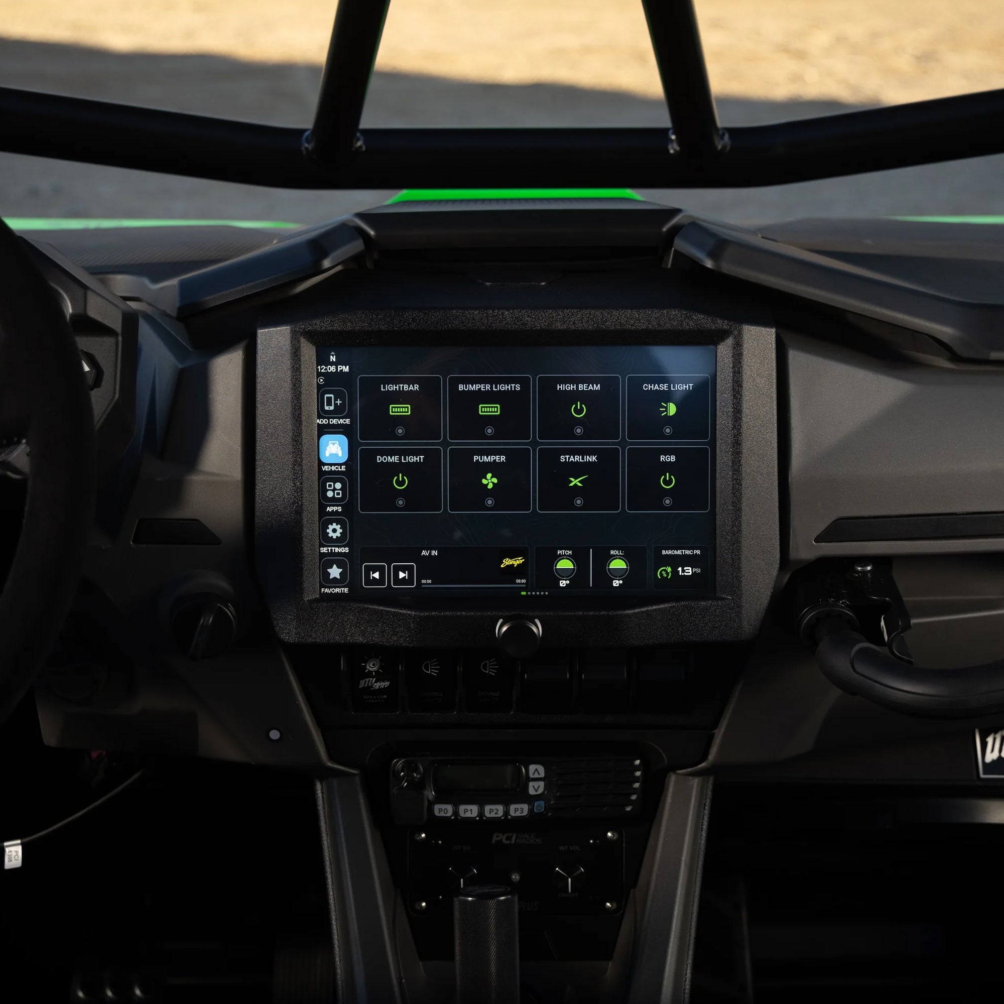 A large rectangular touchscreen display mounted in the center of a vehicle dashboard, showing illuminated app icons and controls. The surrounding cabin is dark gray and black, with part of the steering wheel and gear shifter visible.